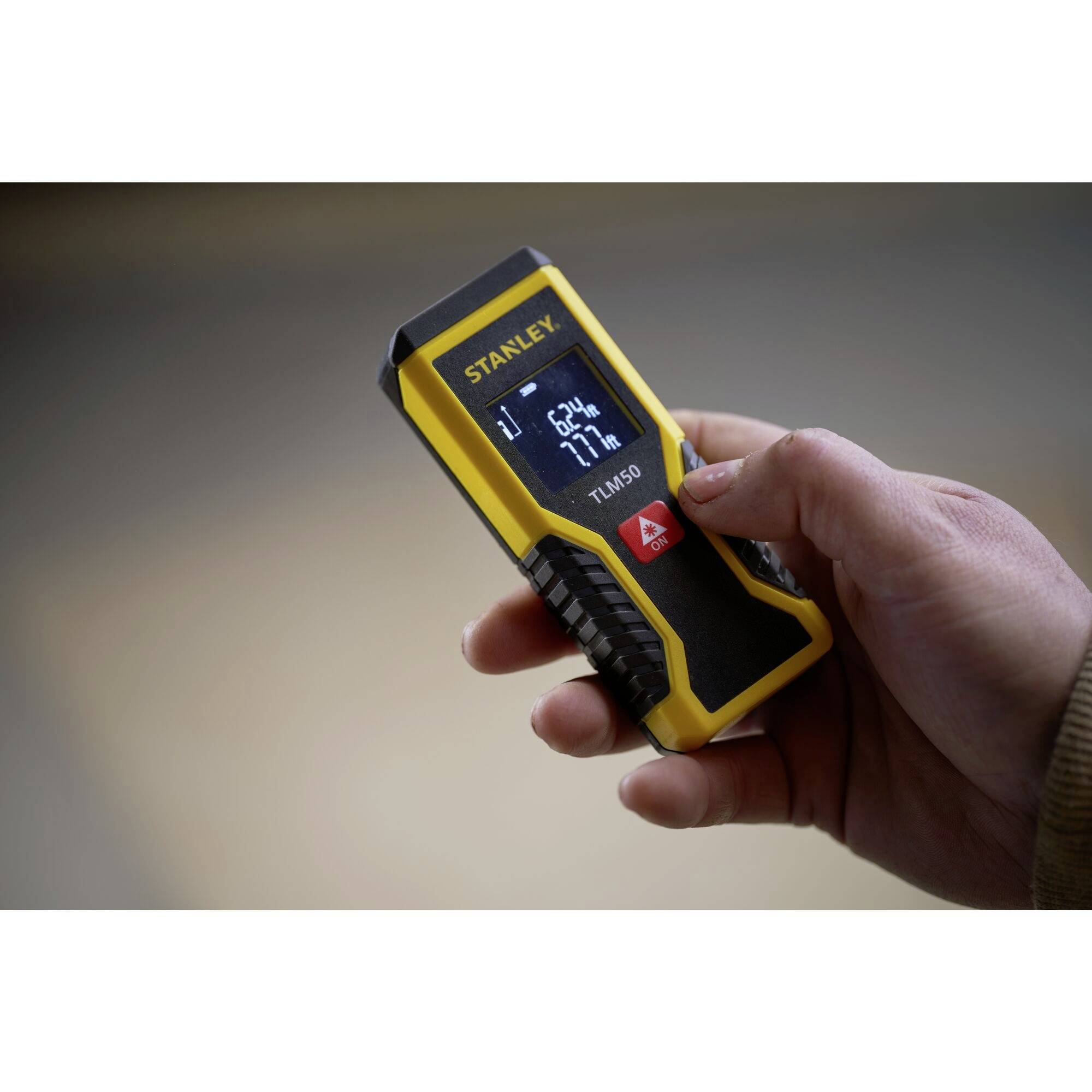 En hand håller ett gult laseravståndsmätningsinstrument med en blå display där '21 m', '67%' och andra data visas.