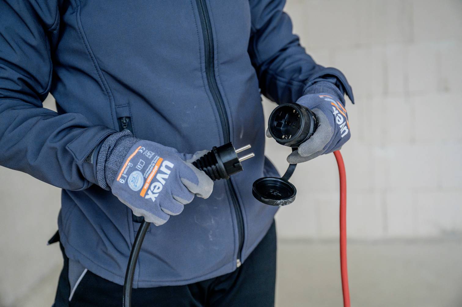 En person i blå jacka och handskar håller två kontakter i händerna, redo att ansluta en svart och en röd kabel.