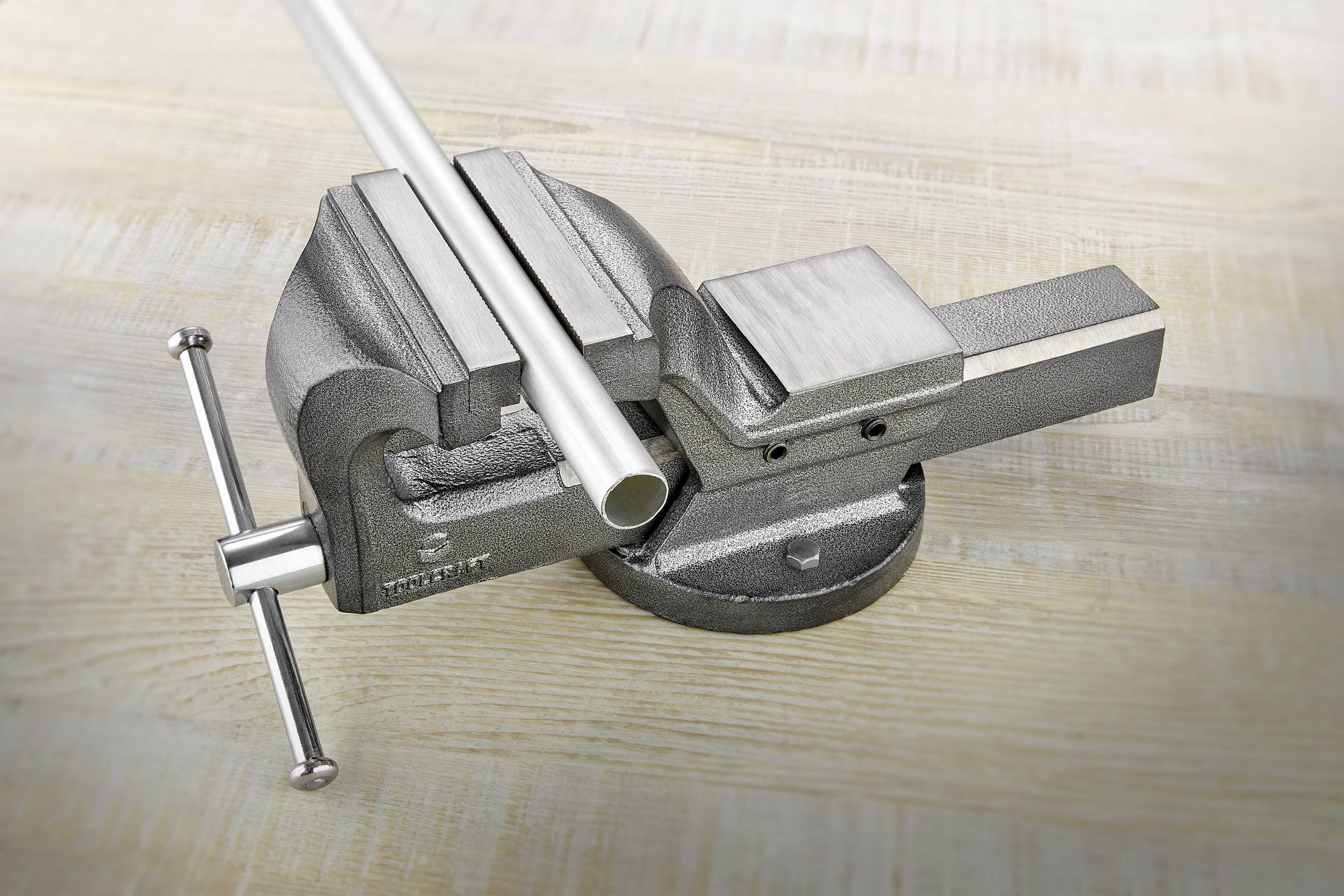 Metallrör som är fastklämt i ett skruvstäd på ett träbord. Röret är horisontellt riktat.