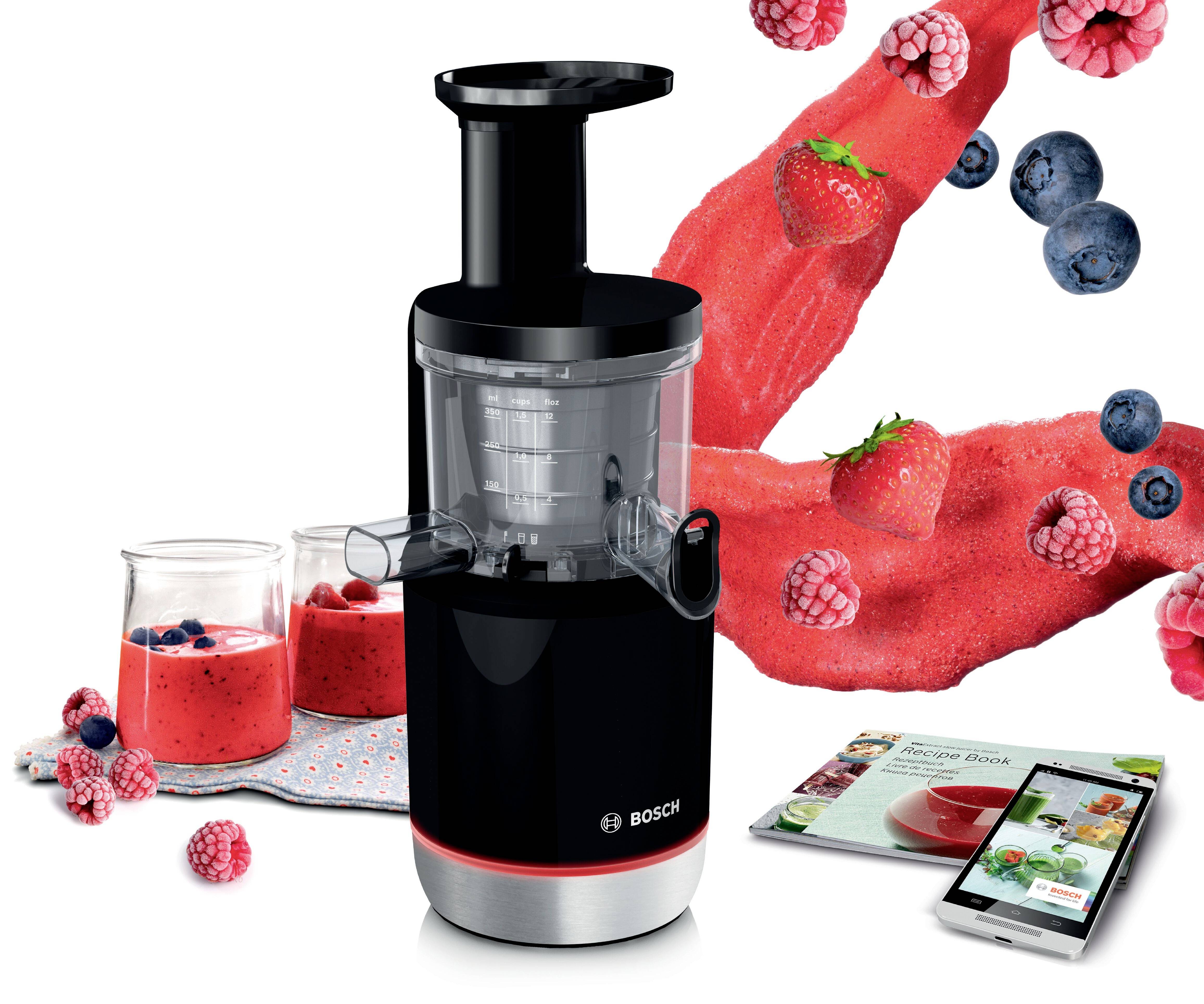 Juicermaskin från Bosch med färska bär och smoothies i bakgrunden; bredvid en kokbok som visar smoothierecept.