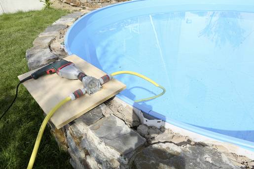 En pool fylls med hjälp av en slang som är ansluten till en pump. Pumpen står på en träplatta vid poolkanten.