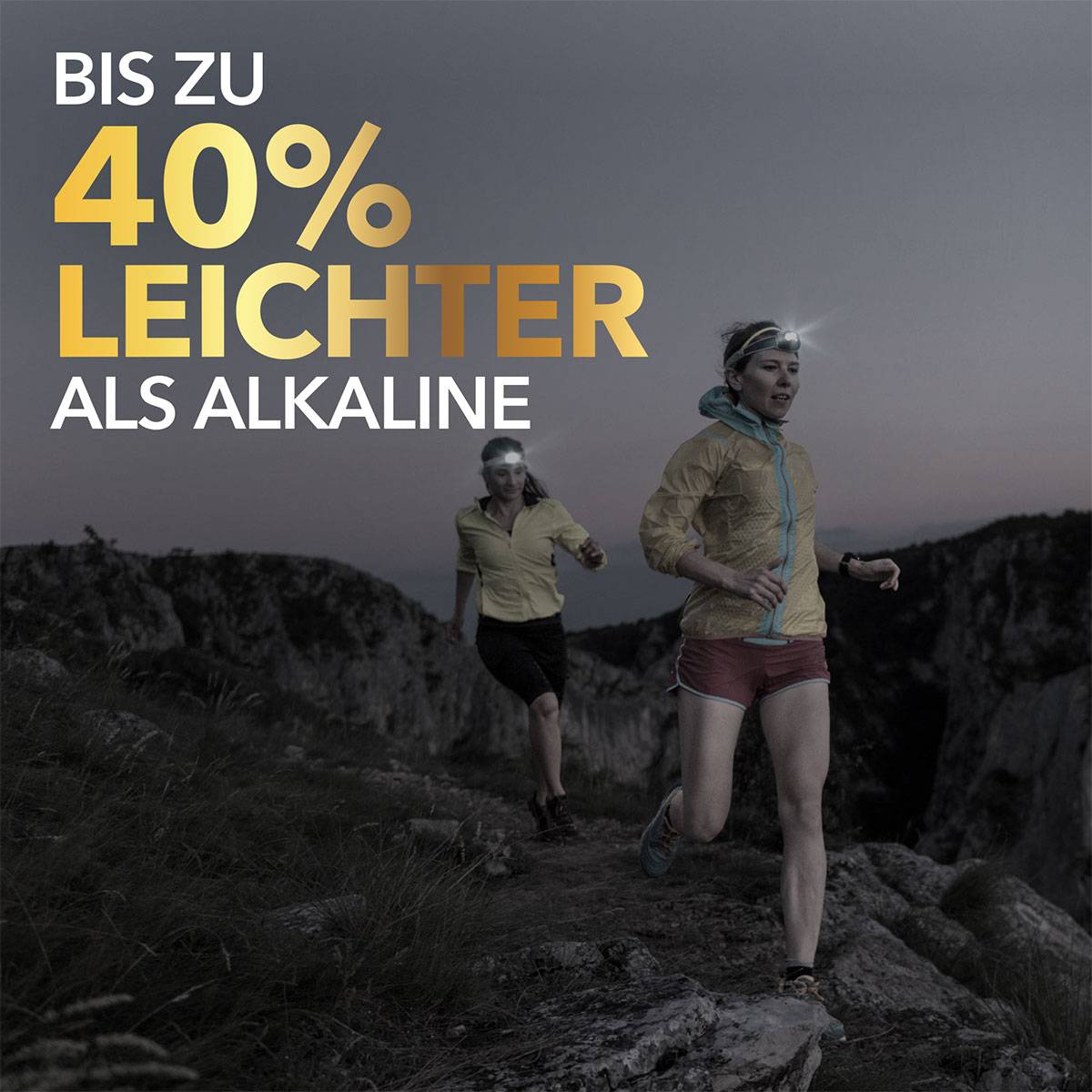 Två kvinnor joggar på natten i ett bergigt landskap, båda bär pannlampor. Text: 'Upp till 40% lättare än Alkaline.'