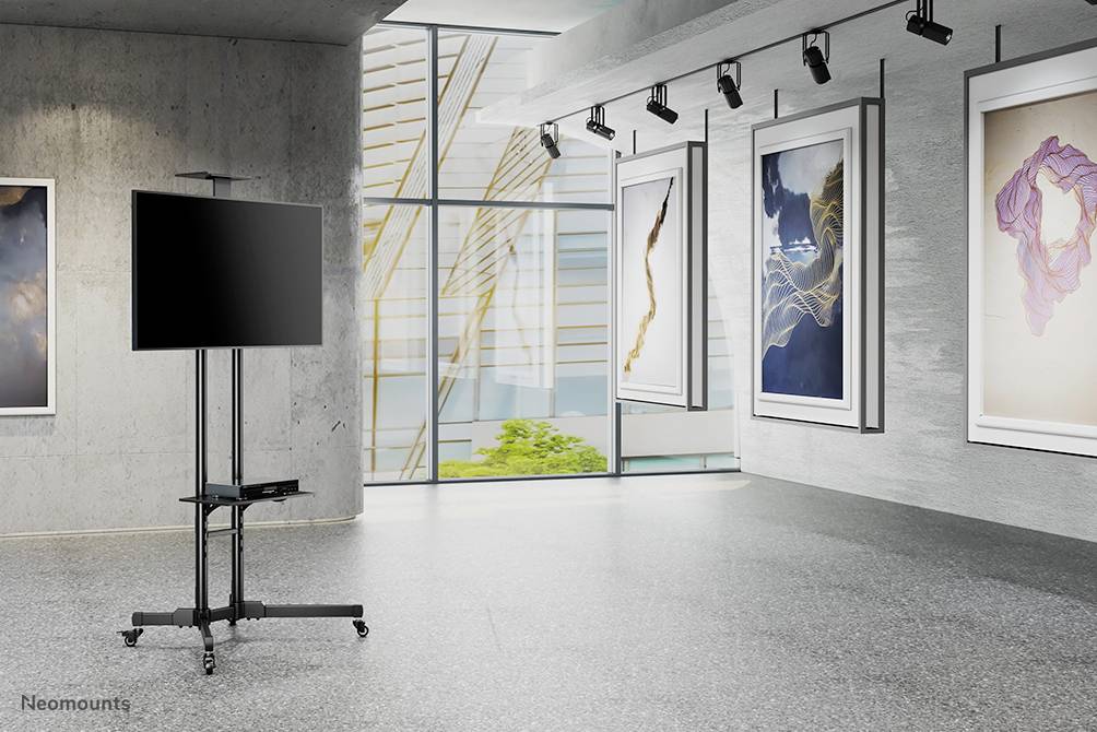 Konstgalleri med ett ljust upplyst rum, flera abstrakta målningar på väggarna och en stor skärm på ett stativ.