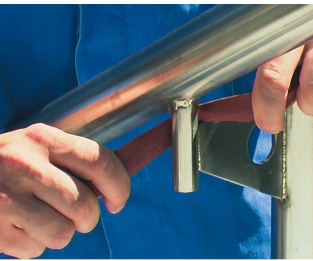 En person slipar ett metallräcke med ett rött slipband. Händer och en del av den blå skjortan syns.