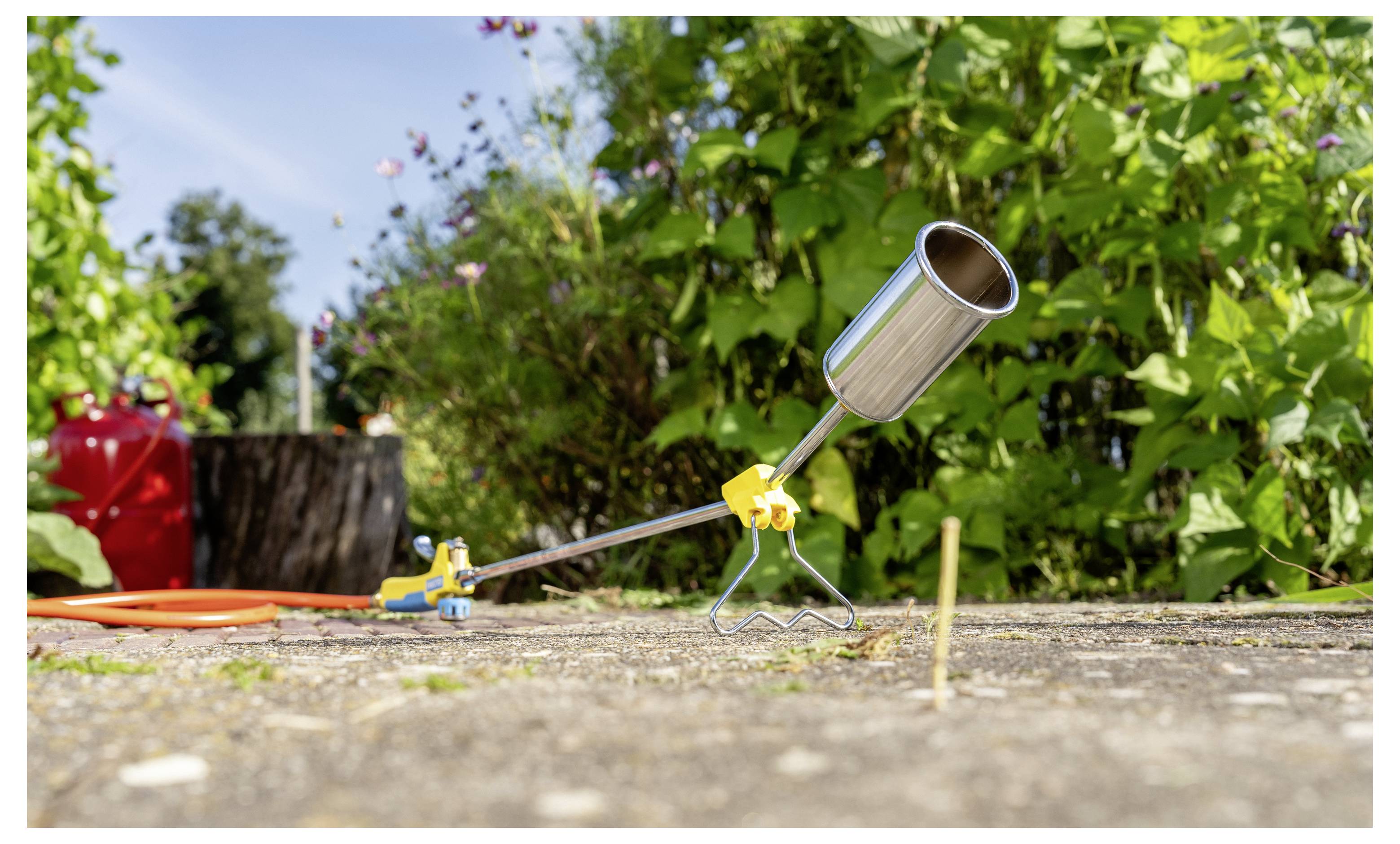 En trädgårdsprinkler på marknivå vattnar växter och sprayer en fin dimma längs en väg bredvid grön lövverk.