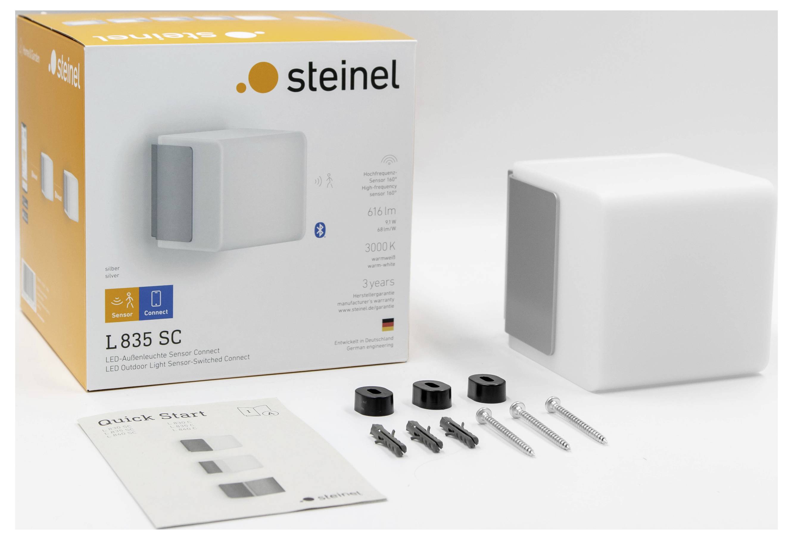 Steinel L 835 SC LED-utomhusbelysningspaket med låda, vit vägglampa, snabbstartsguide och monteringsutrustning på en vit bakgrund.