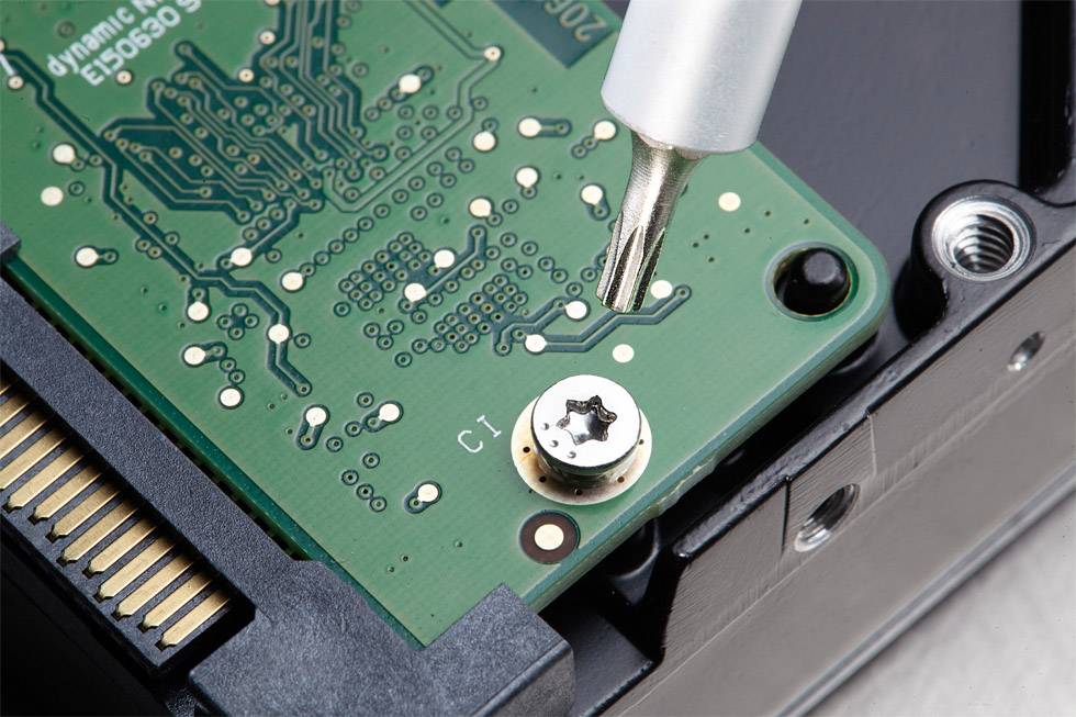 Närbild av ett grönt kretskort med ett metallverktyg som drar åt en skruv. Till vänster syns en del av en elektronisk kontakt.