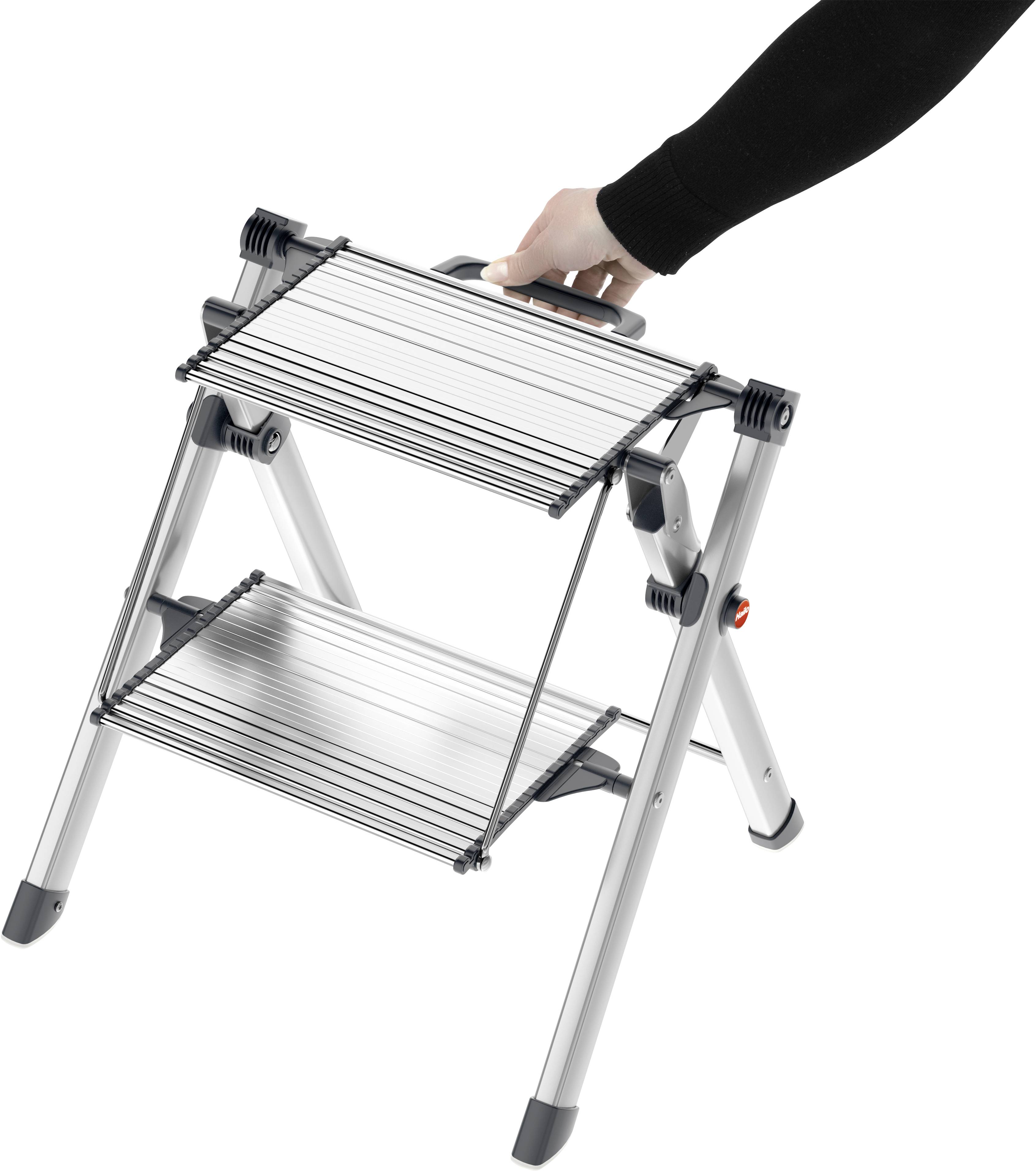 Silvrig fällbar stege med två steg och ett svart handtag, hållen av en hand. Stegen är kompakt och bärbar.