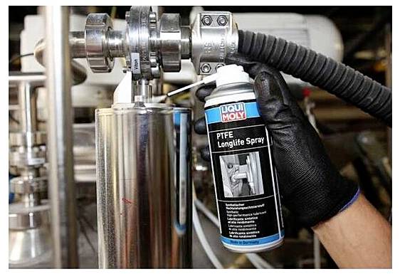 En person som bär en svart handske använder "Liqui Moly PTFE Longlife Spray" på industriella maskiner, troligtvis för smörjning eller underhåll.