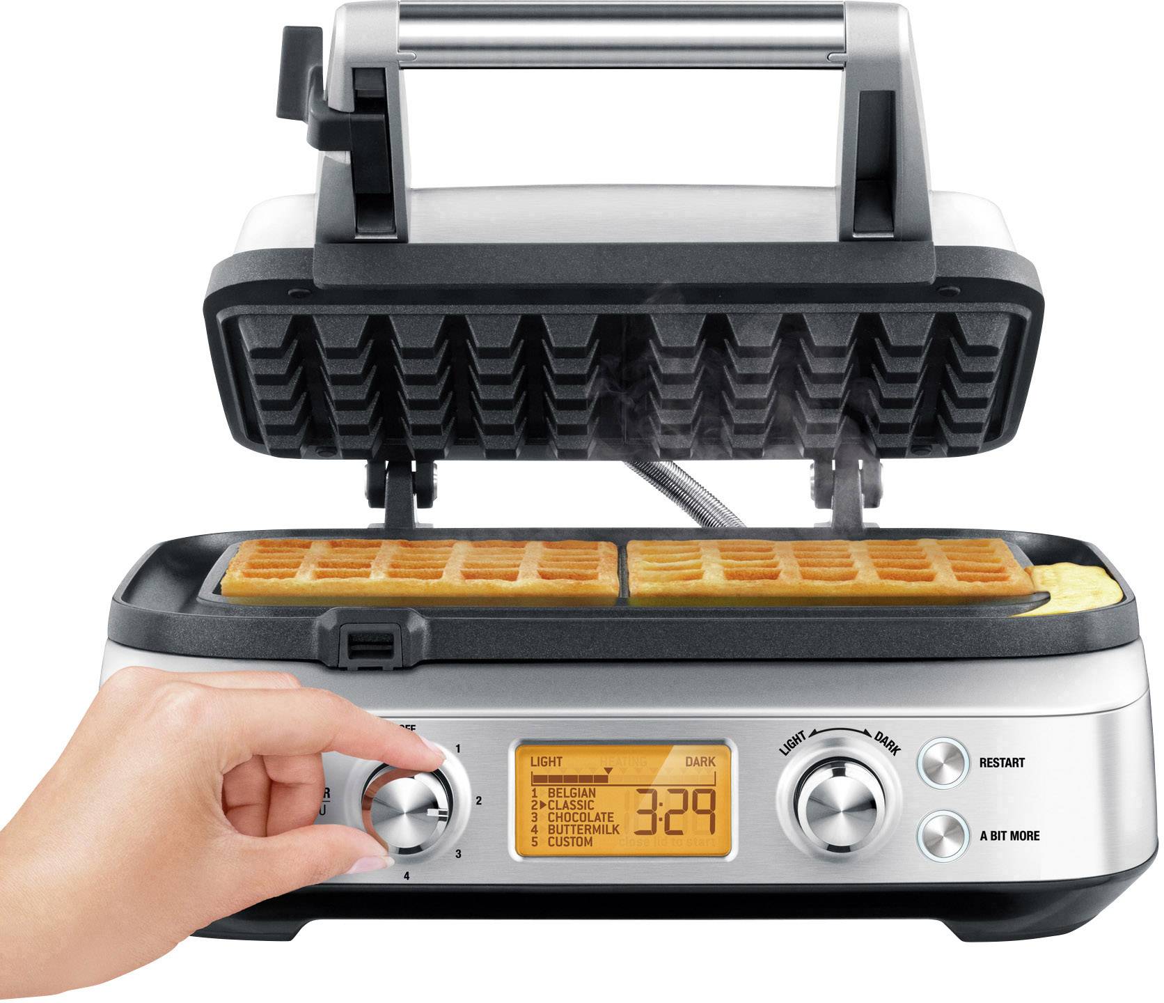 En våffeljärn med öppnat lock där våfflor bakas. En hand vrider på knappen för att justera brynivån.