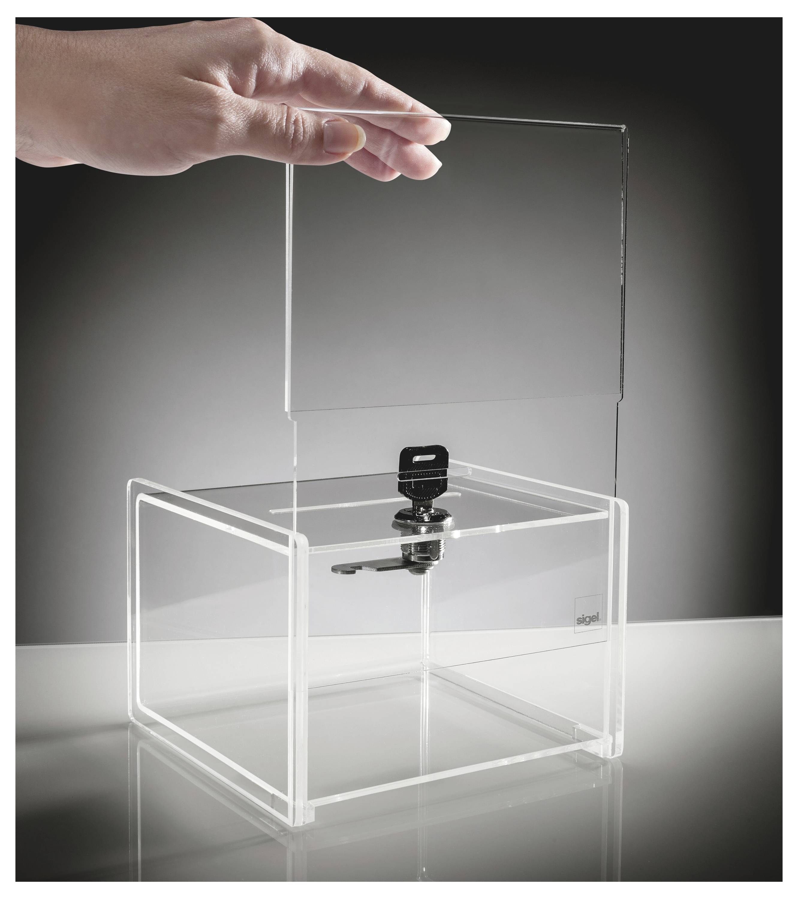 Hand som placerar ett klart akrylllock på en transparent displaybox med ett centralt svart lås eller spärr.