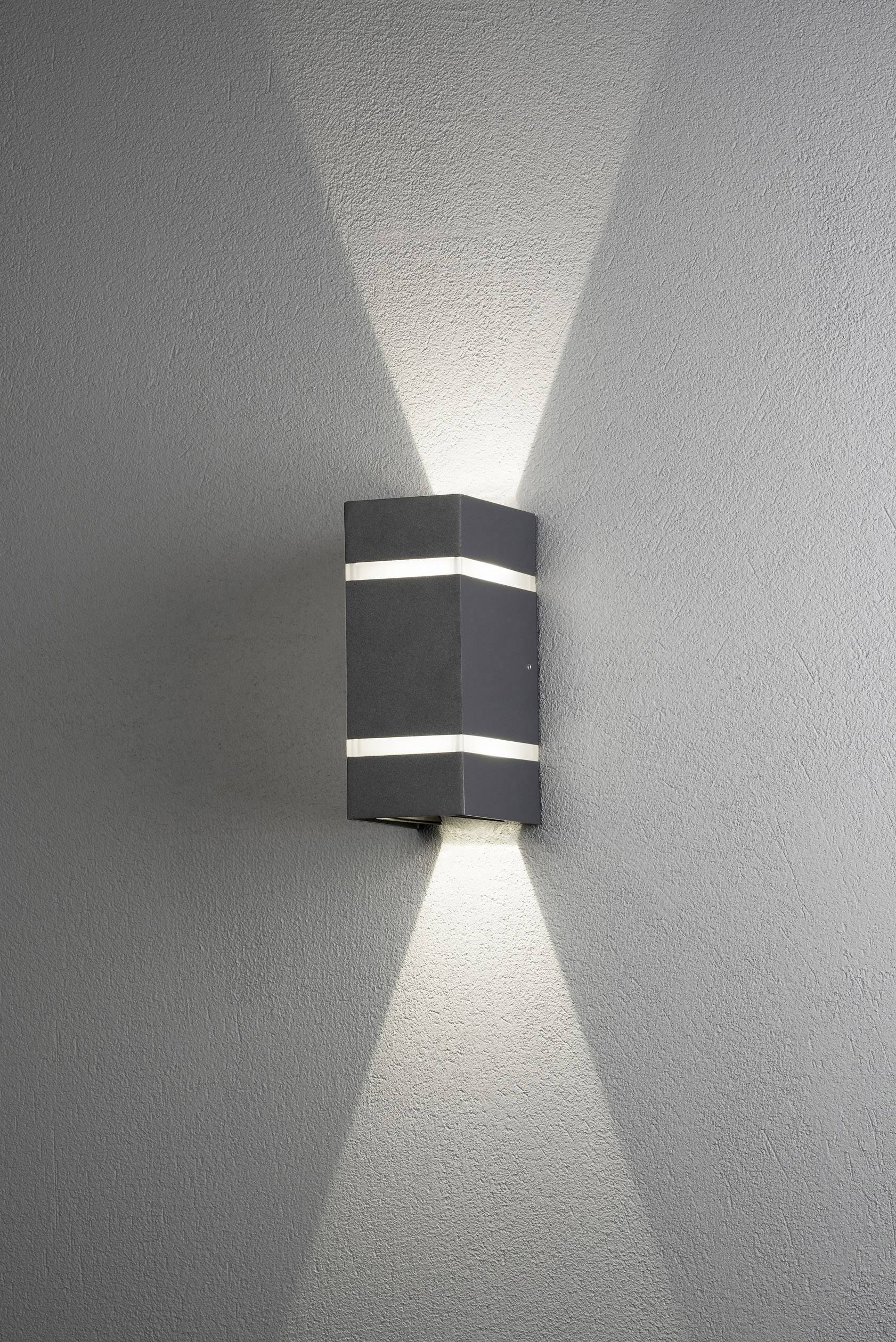 En rektangulär, svart vägglampa lyser uppåt och nedåt och skapar ett symmetriskt ljusmönster på den grå väggen.