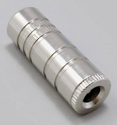 En cylinderformad, silverfärgad metalladapter med räfflad yta och ett hålrum i mitten, ligger på en grå yta.