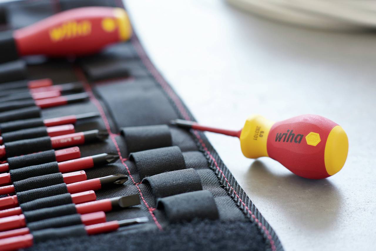 En uppsättning röda skruvmejslar med gula handtag ligger på ett bord; en har tagits ut separat. Märke: Wiha.