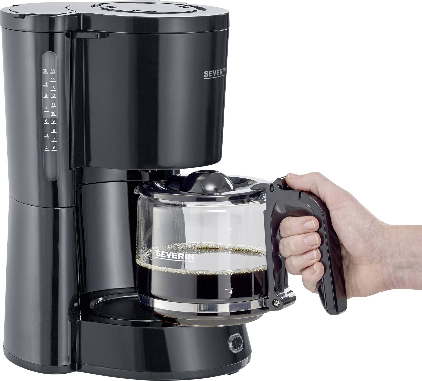 En hand håller glaskannans från en svart kaffebryggare som innehåller nybryggd kaffe.