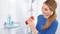 En kvinna i en blå tröja kontrollerar en röd schampoflaska i ett badrum med vita kakel och en duschslang i bakgrunden.