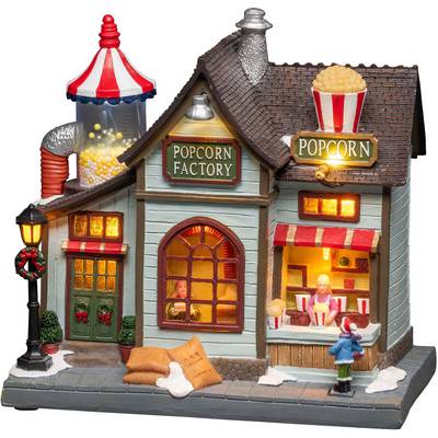 Upplyst miniatyrbyggnad med texten 'Popcorn Factory', visar en kiosk där en figur serverar popcorn.