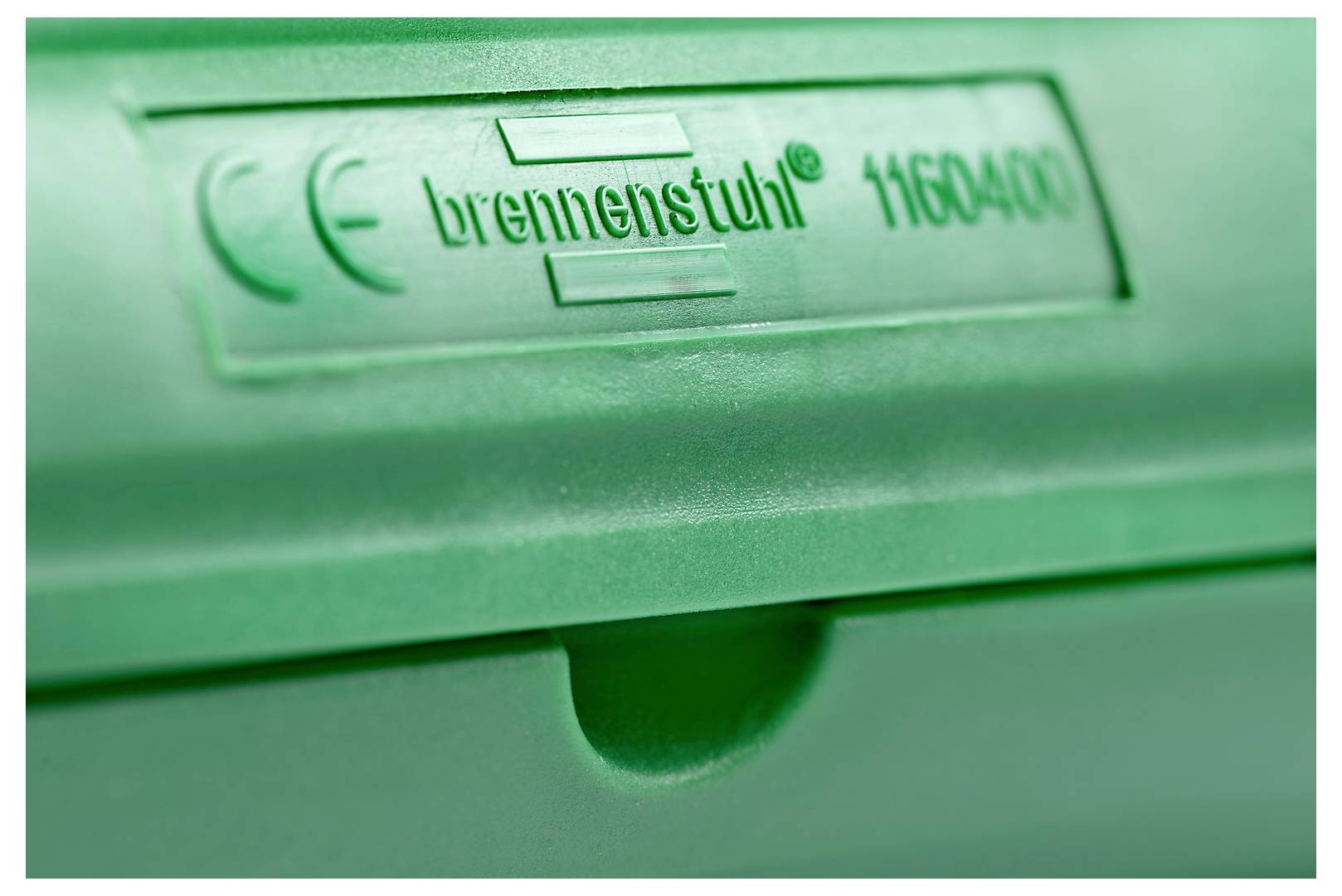Närbild av en grön plastisk enhetsetikett med texten "brennenstuhl 116840" med CE-märkning och ett centralt skåra nedanför.