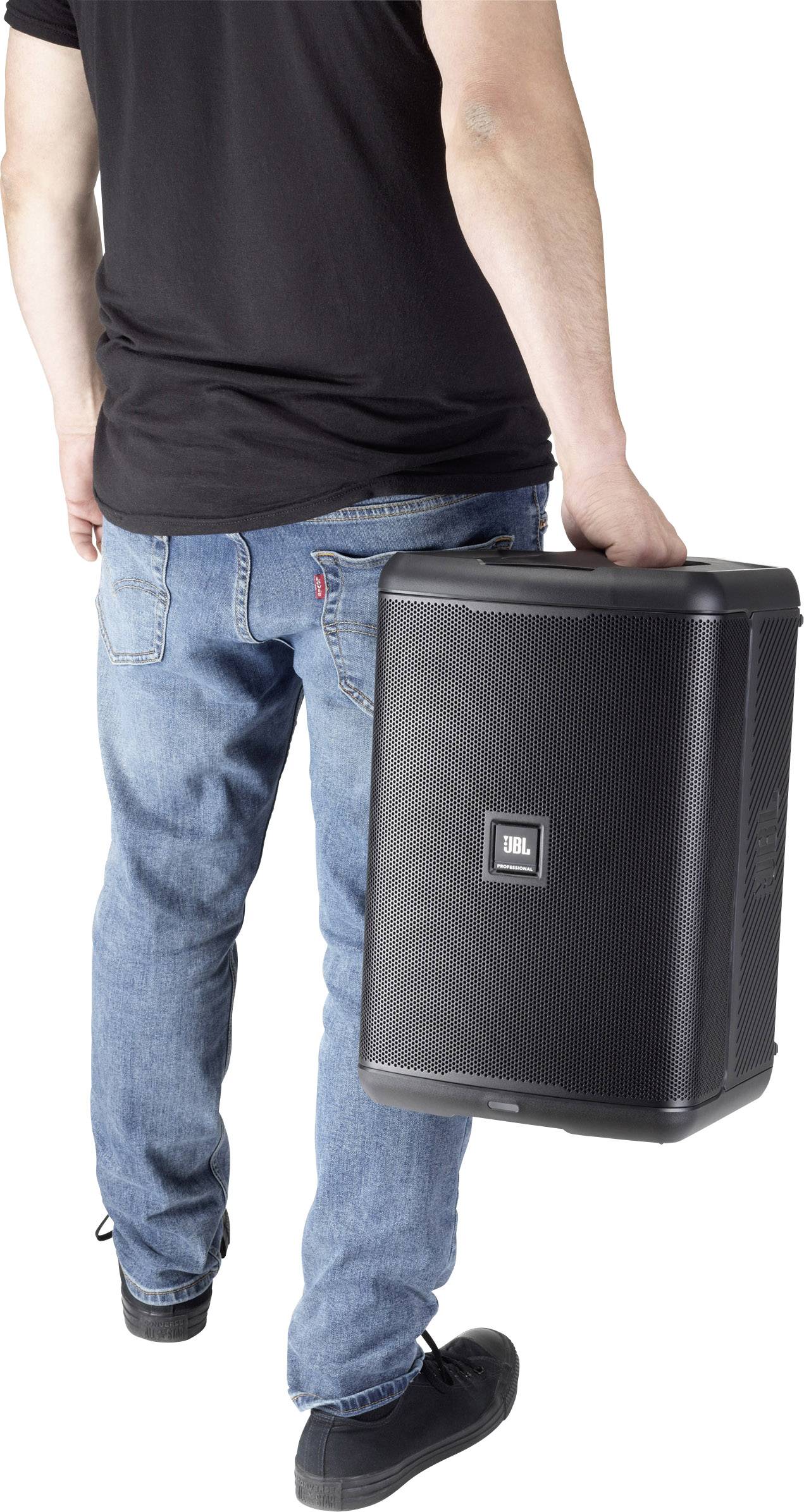 En person bär en stor högtalare i höger hand. Personen har jeans och en svart t-shirt.