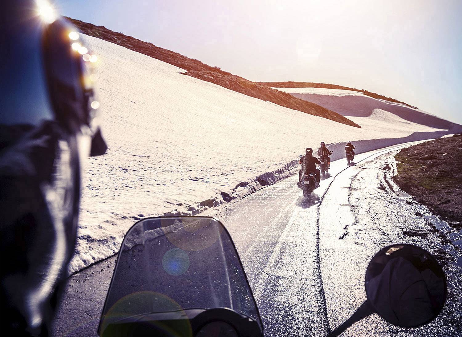 Motorcyklist på en snötäckt bergväg, i solljus. Vägen är våt, vilket skulle kunna tyda på en nyligen inträffad snösmältning.