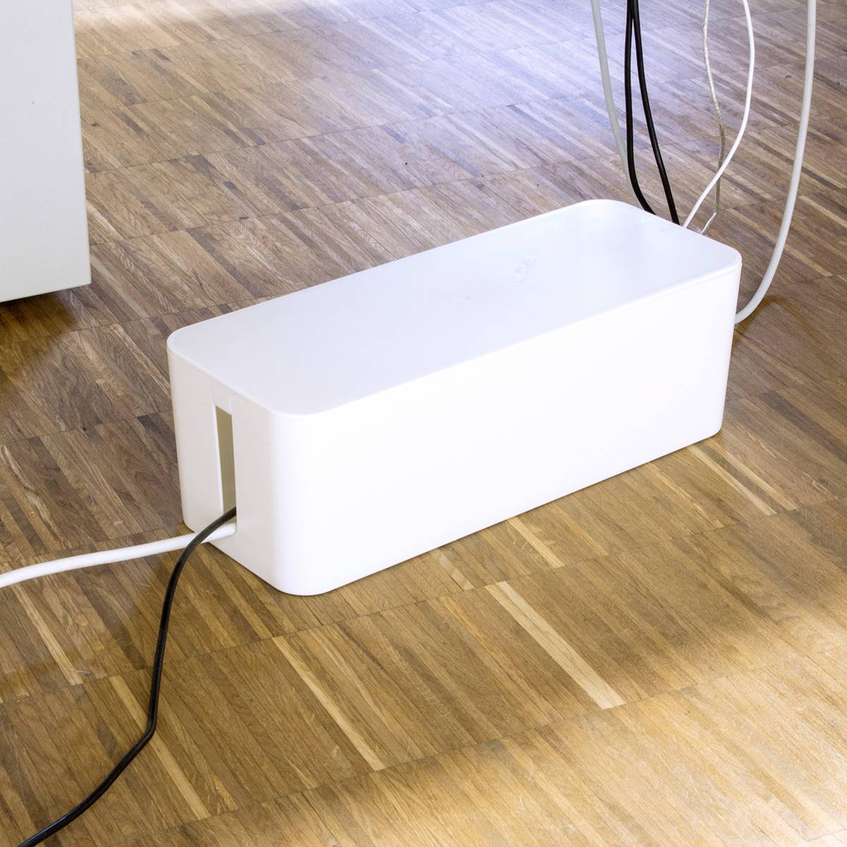 En vit kabelbox på ett trägolv som organiserar och döljer kablar.