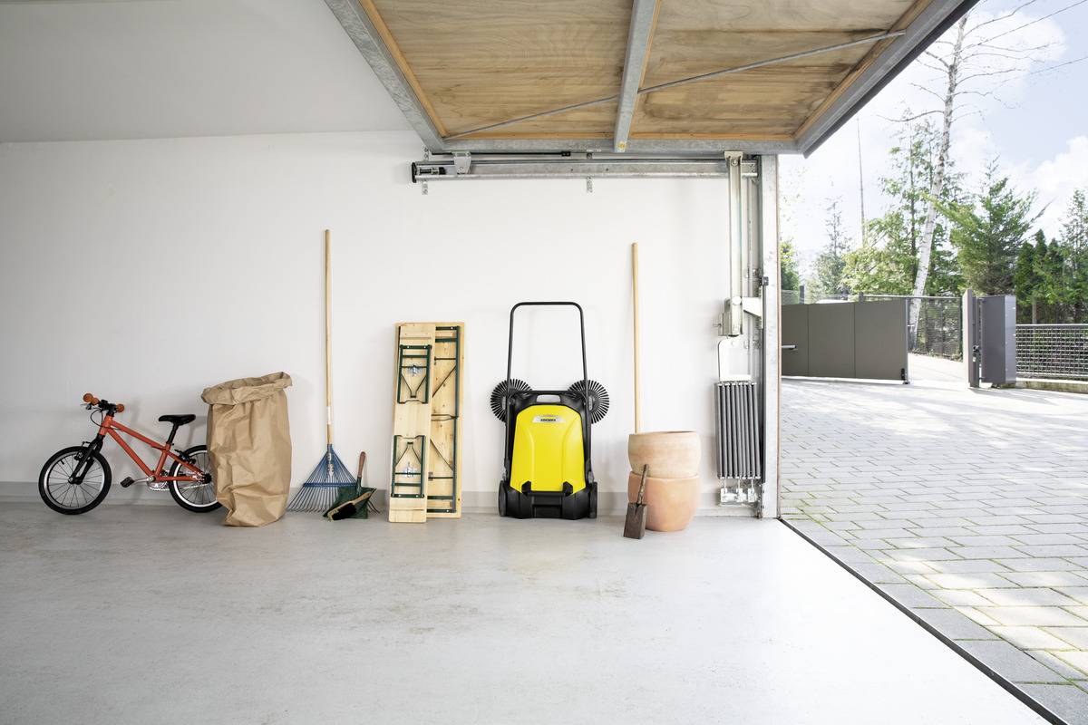 Ett välorganiserat garage med ett barncykel, trädgårdsredskap, en papperspåse, en ihopvikt stol, en gul städmaskin och en stor blomkruka.