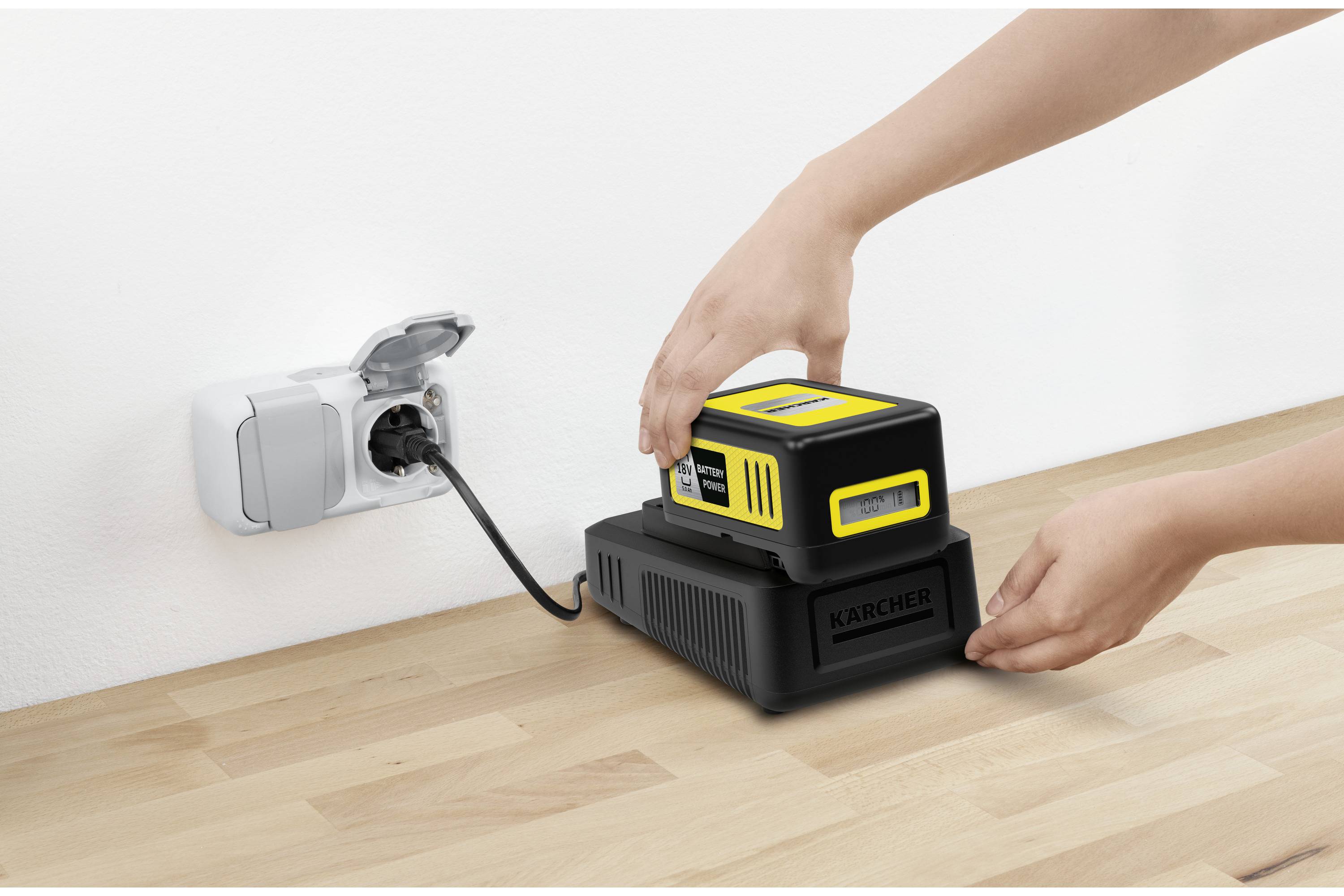 En person laddar ett gult batteri med en svart laddningsstation som är ansluten till ett eluttag.