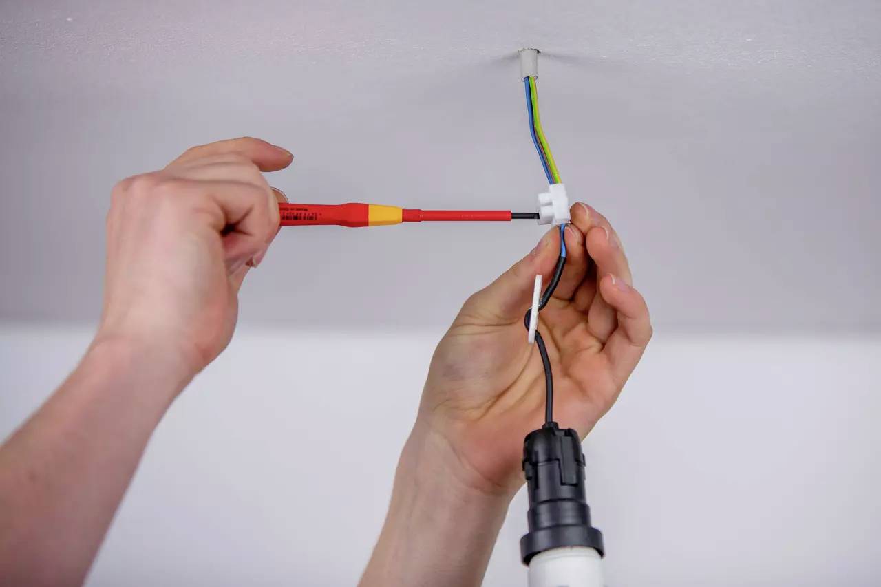 En person installerar en taklampa. En hand håller i en skruvmejsel medan den andra ansluter ledningar.