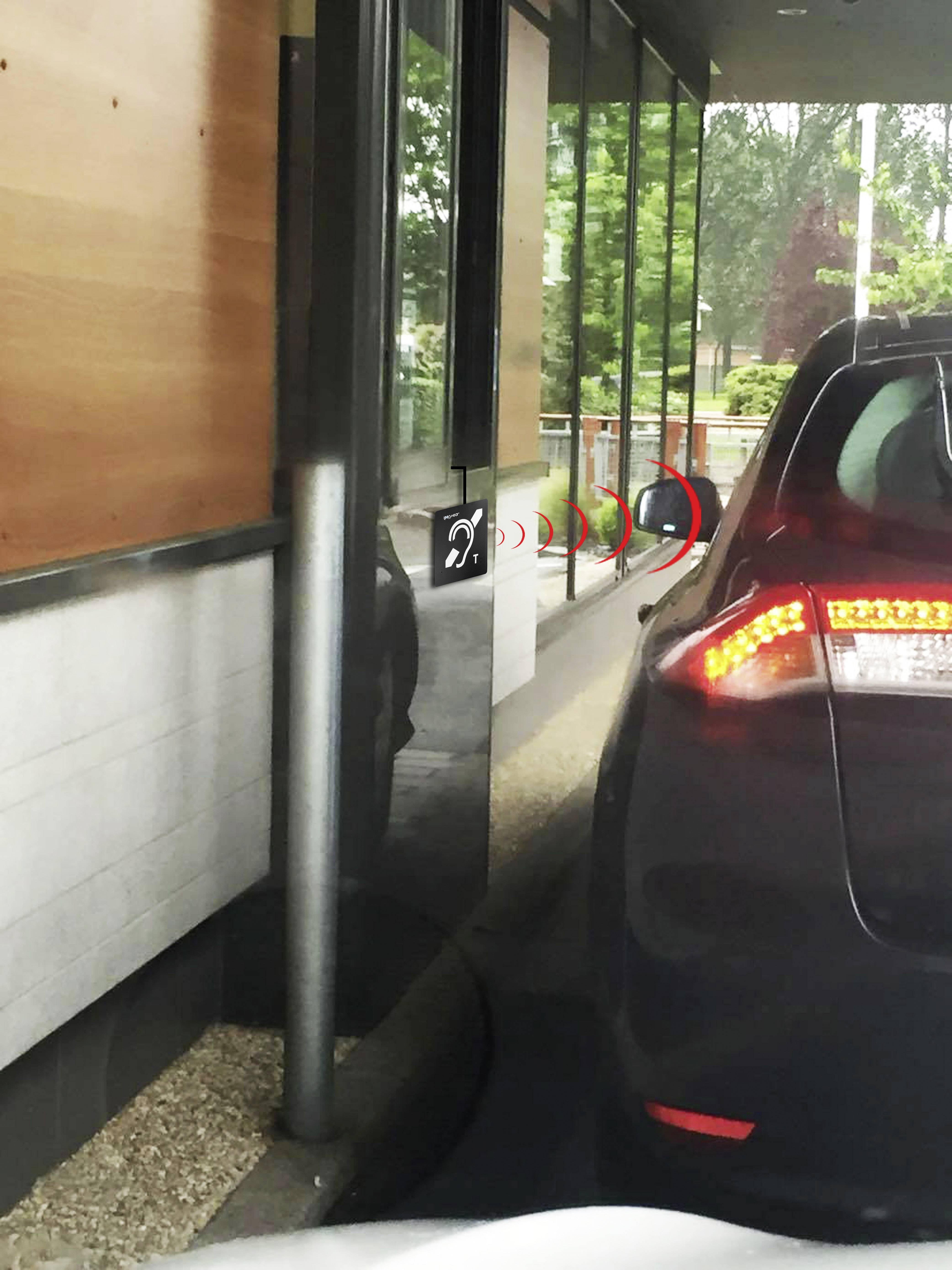 Bil i drive through-kön vid en restaurang, stannar vid en diskret placerad högtalare för att göra sin beställning, som är svår att urskilja.