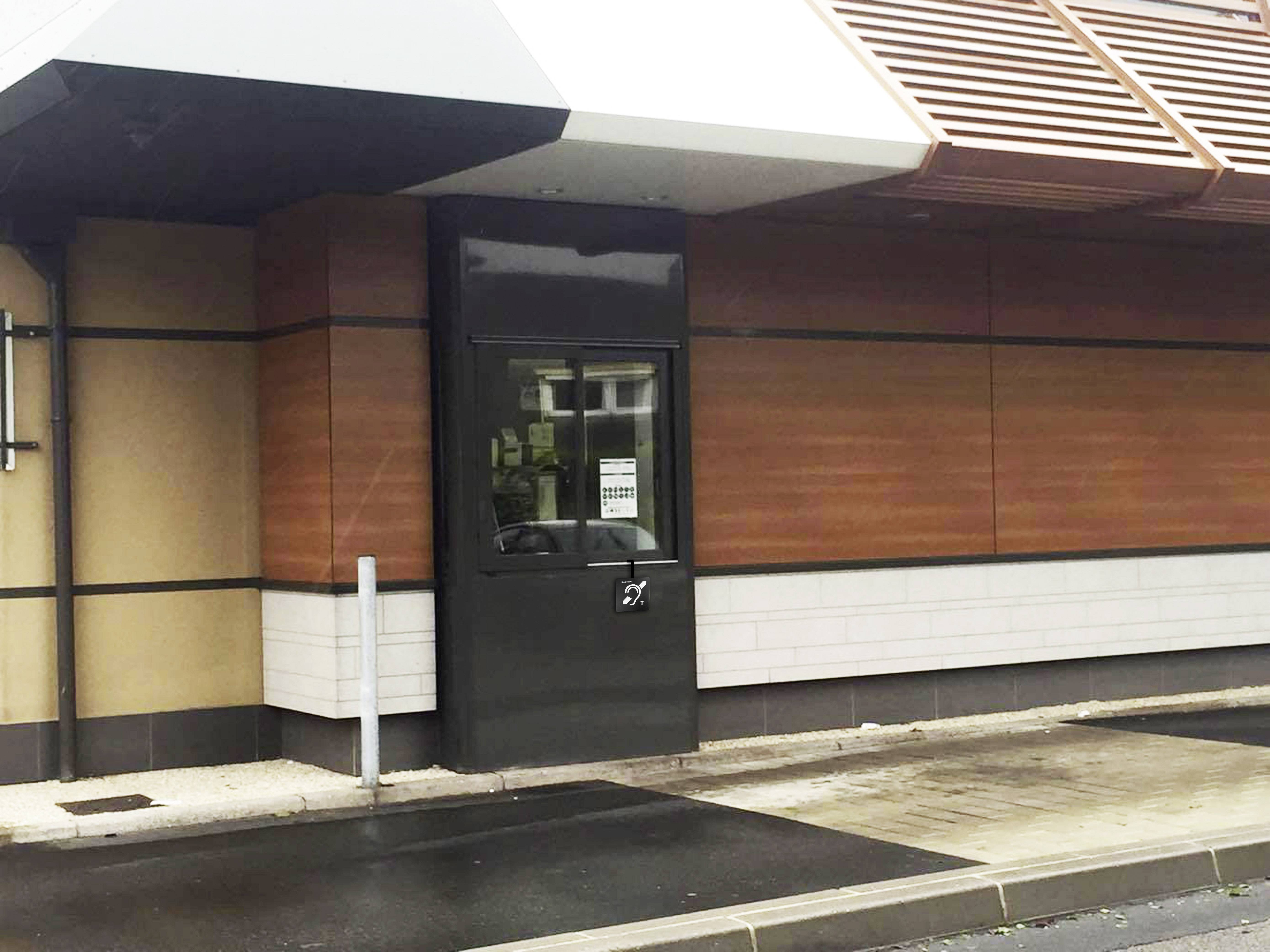 Ett stängt drive-in-fönster på en snabbmatsrestaurang, omgivet av en modern trä- och metallfasad.
