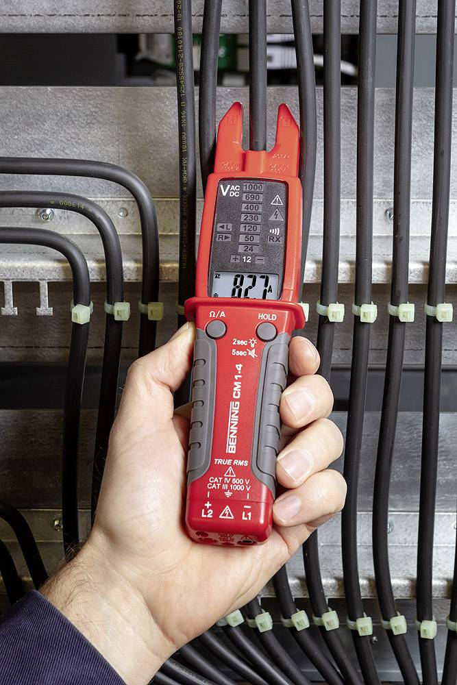 En hand håller ett digitalt spänningsmätinstrument mellan flera svarta kablar. Displayen visar mätvärdet.