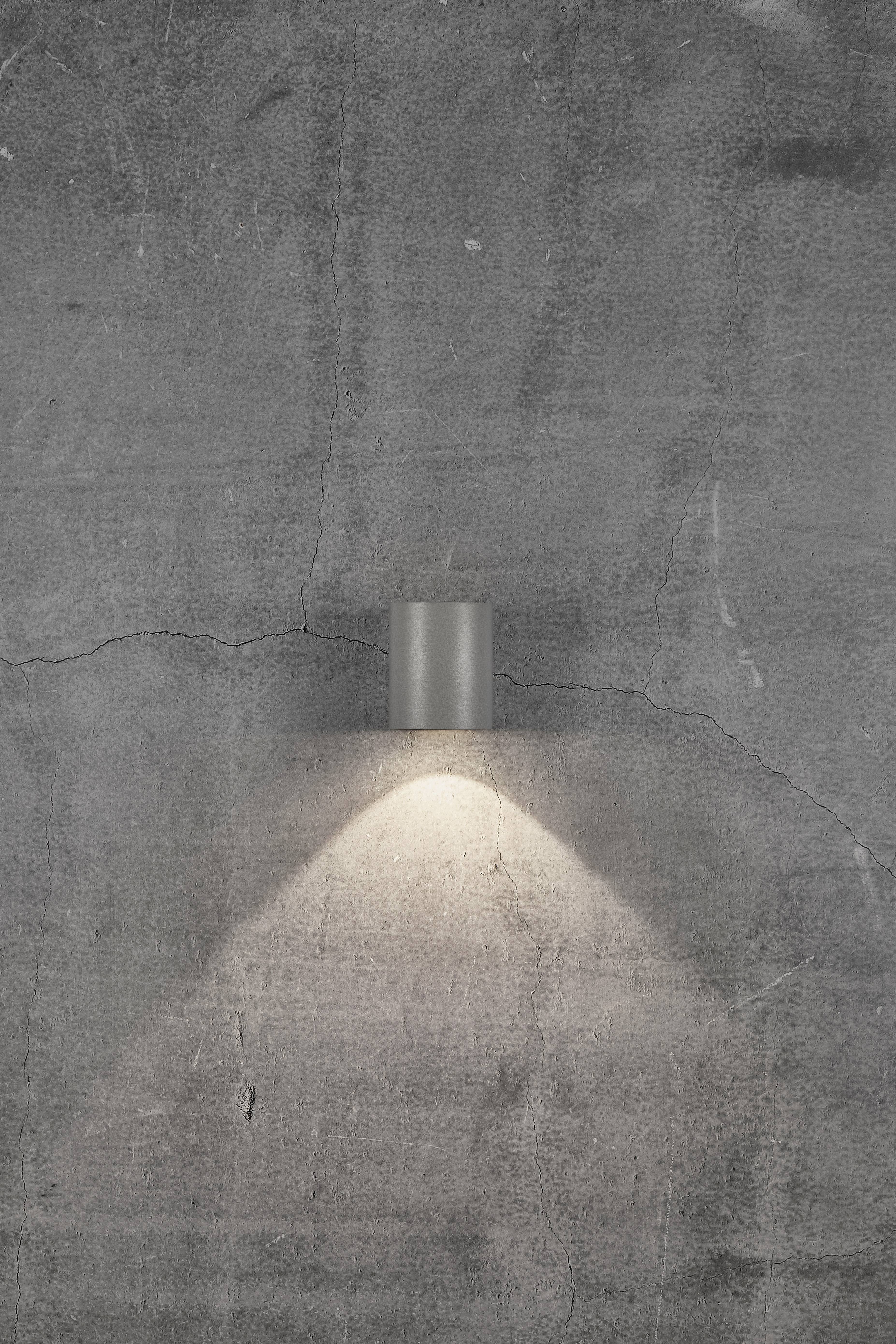 Vägglampa på en grå, strukturerad betongyta, lyser svagt nedåt.