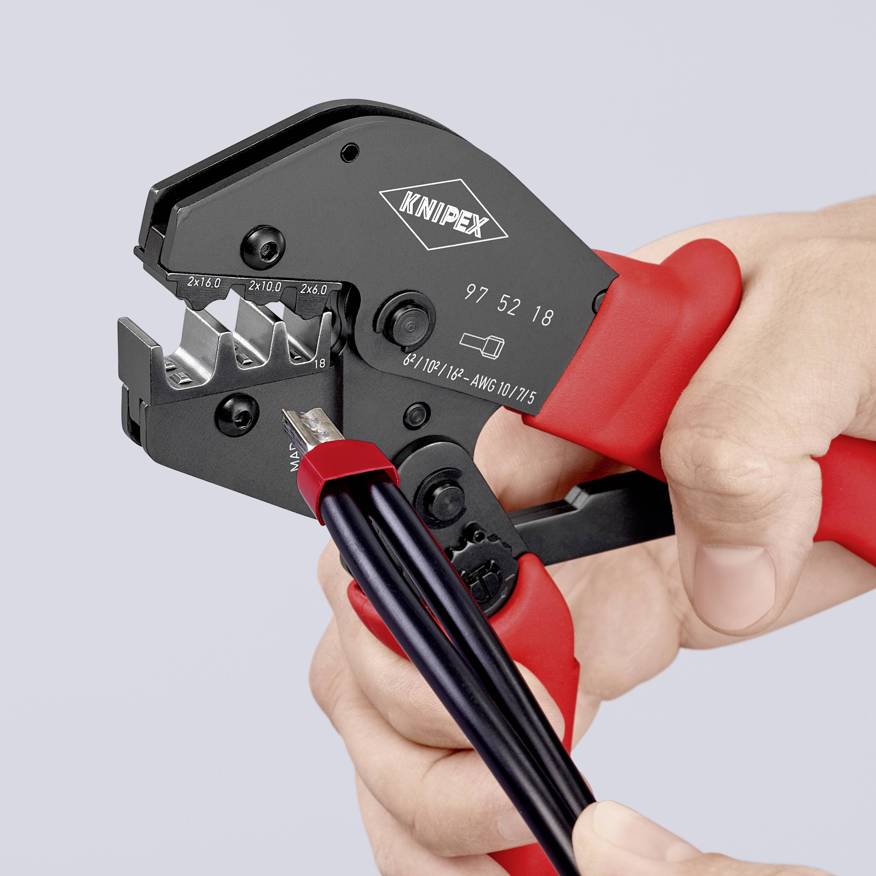 En hand använder en röd Knipex-krympningstång för att krympa en kabel.