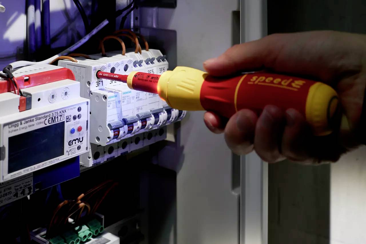 Hand håller skruvmejsel vid en säkringsdosa och visar på elektriskt arbete.