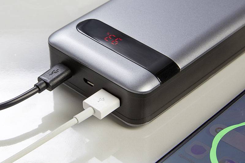 En powerbank laddar en smartphone. Två kablar är anslutna; en visar till en närliggande smartphone med aktiverad skärm.