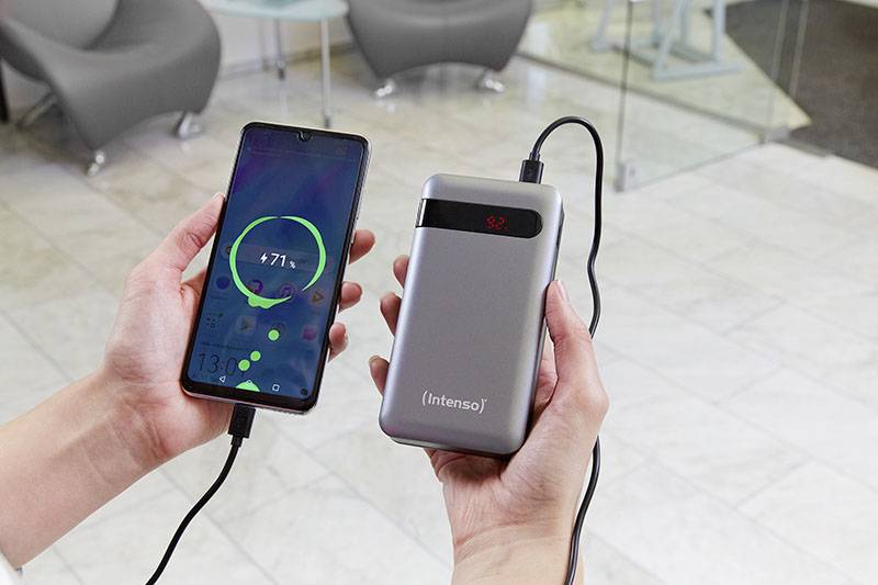 En person håller i en smartphone som är ansluten till en bärbar powerbank via en kabel. Smartphonen visar en pågående laddning.