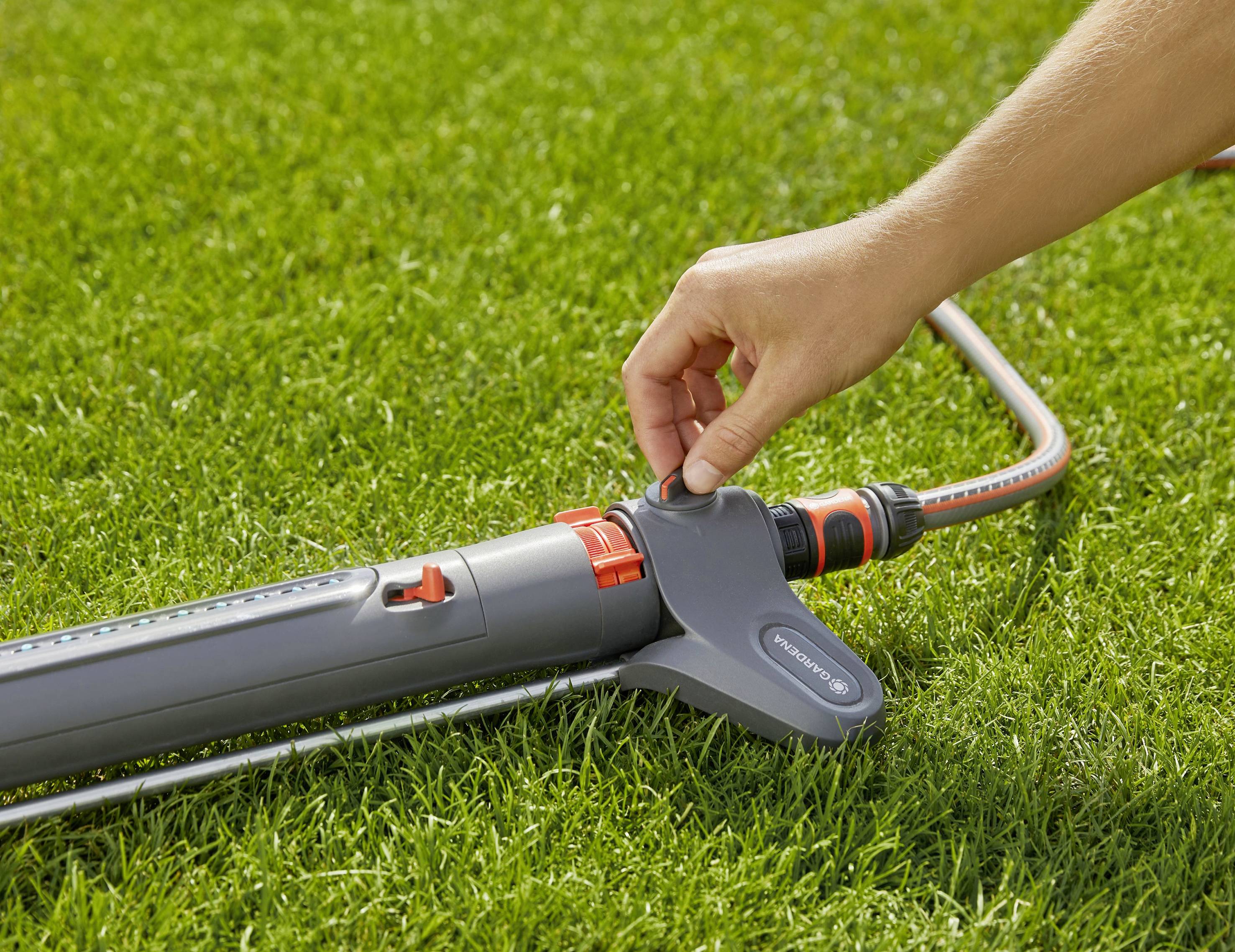 En person justerar vattenflödet från en trädgårdssprinkler på en gräsmatta.