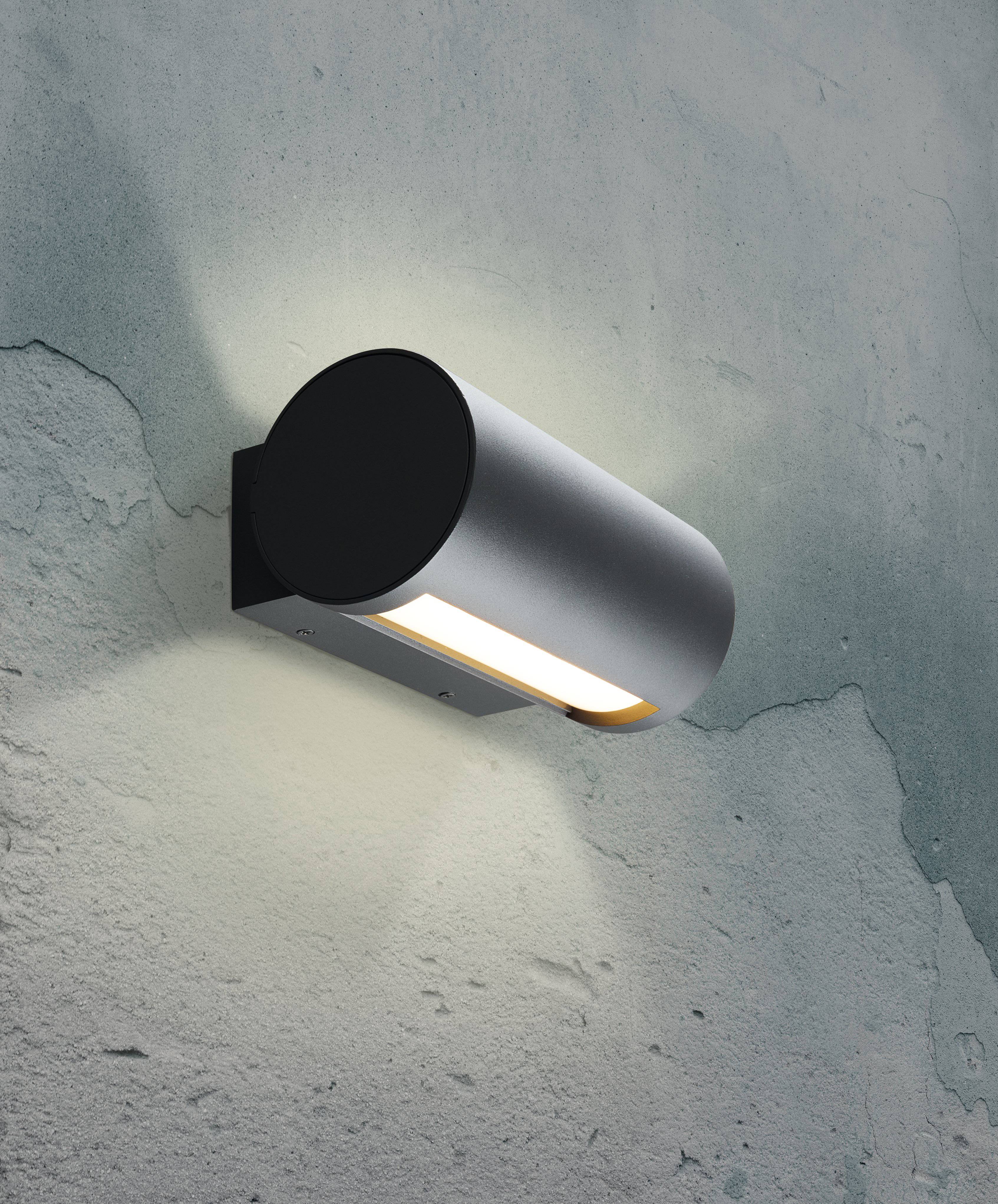 Vägglampa på en betongvägg som sprider ett diffust, varmt ljus och mjukt belyser omgivningen.