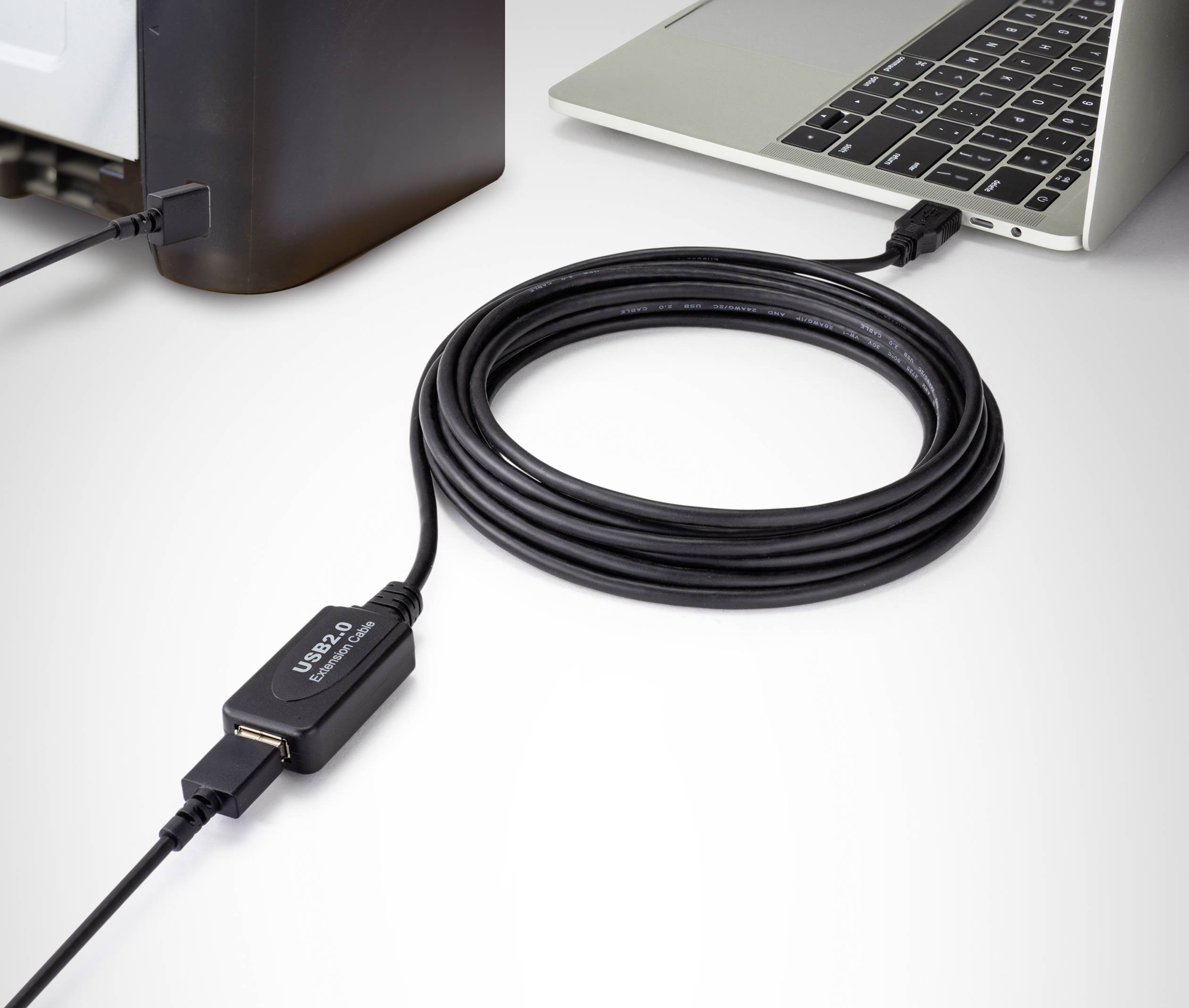 Ett svart USB 2.0-förlängningskabel förbinder en bärbar dator med en annan enhet. Kabeln är upprullad på ett bord.