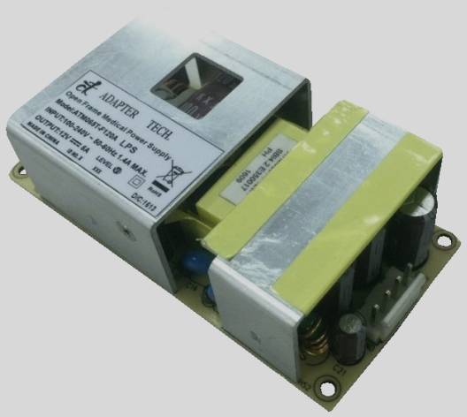 Ett öppet nätaggregatsmodul med elektroniska komponenter och en etikett ovanpå. Etiketten visar tekniska specifikationer för nätaggregatet.