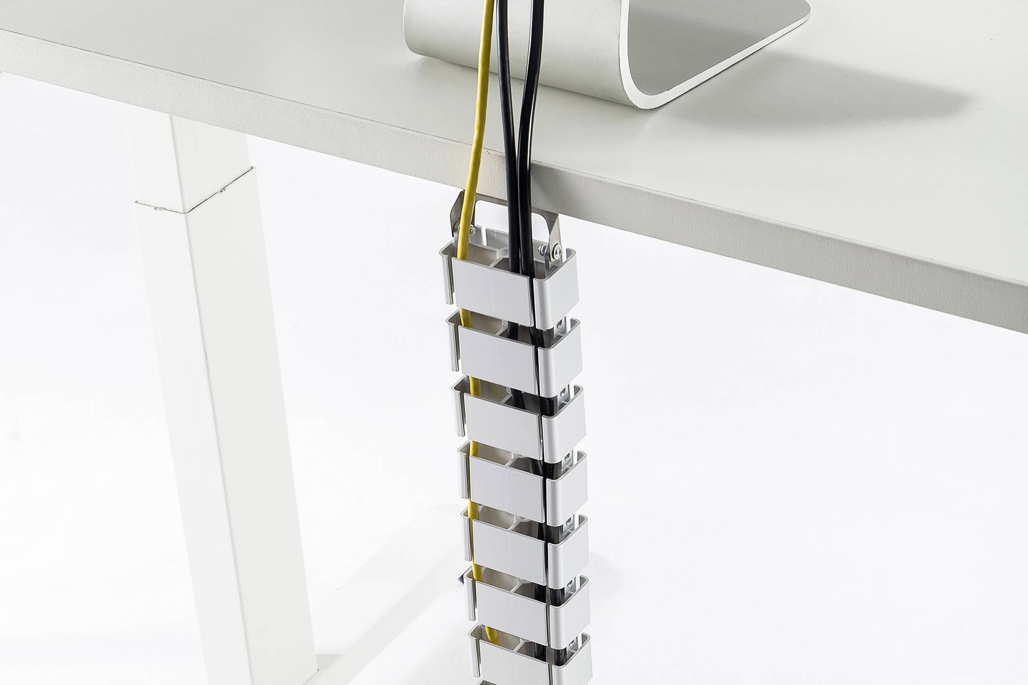 Kabelhanteringsystemet håller flera kablar organiserade och säkra längs ett vitt bordsben.