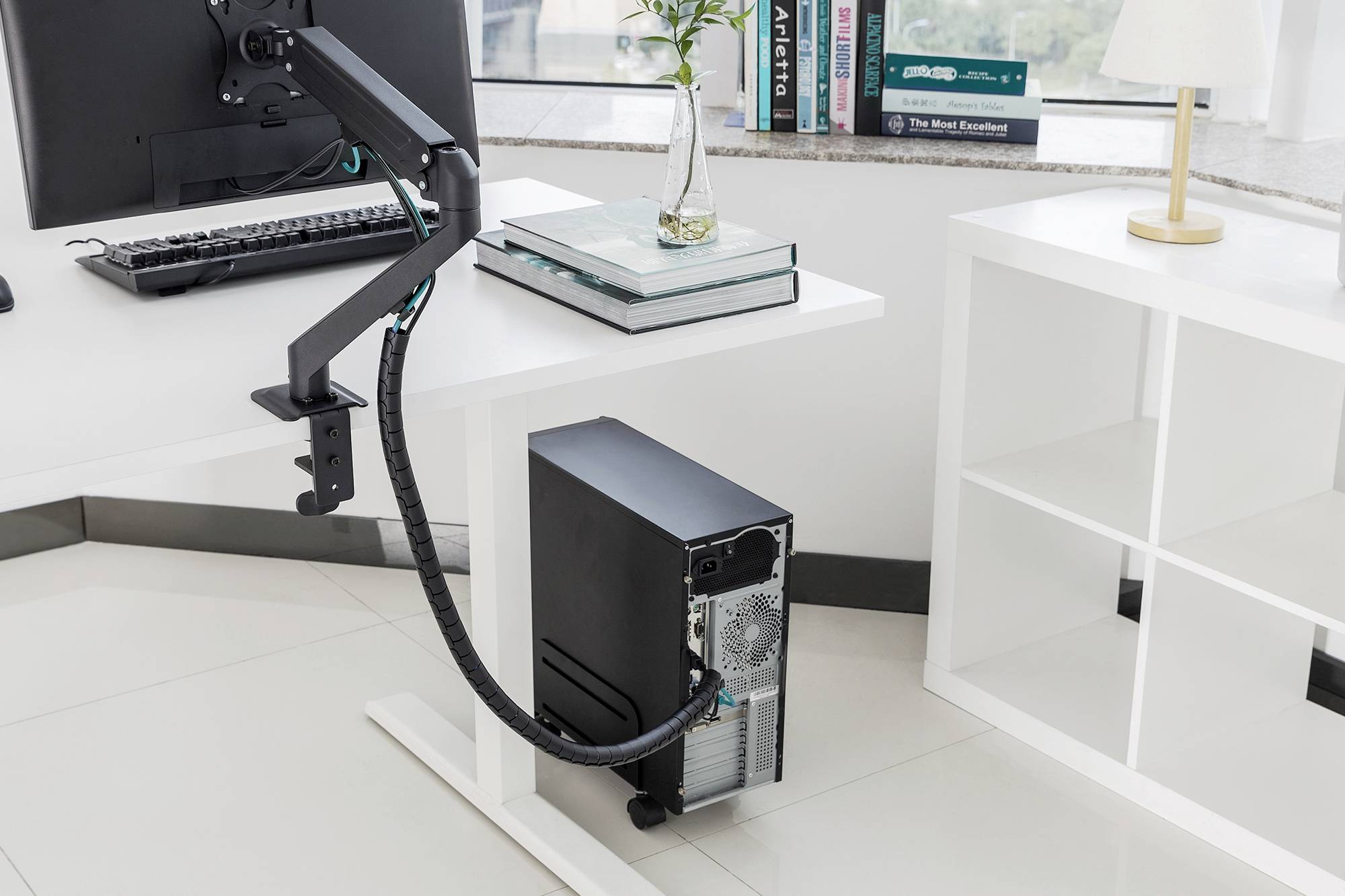 En dator med ett kabelhanterings­system står på ett skrivbord i ett modernt kontor. Böcker och lampa i bakgrunden.