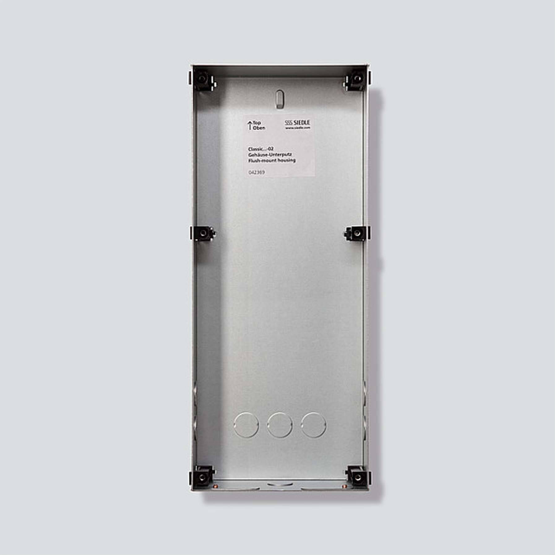 Tomt elektriskt hölje av silverfärgad metall, rektangulärt; fyra fästdetaljer på sidorna.
