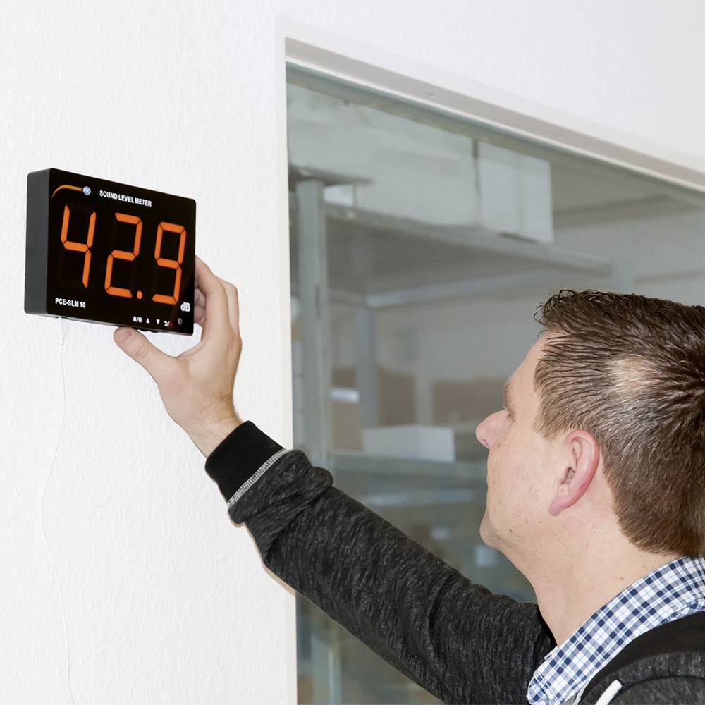 En man kontrollerar ett vägginstrument som visar en ljudnivå på 42,9 decibel.