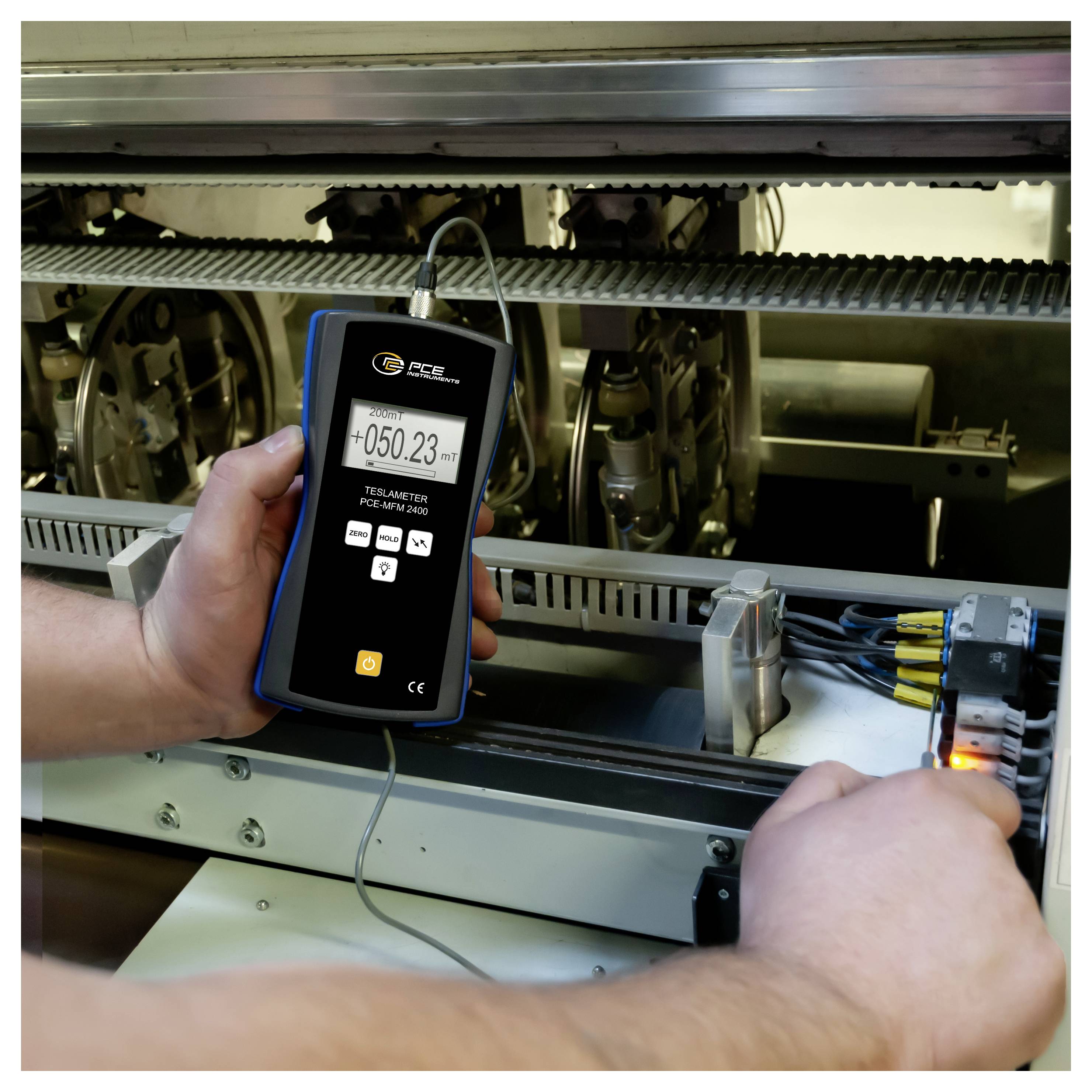 En tekniker använder ett handhållet telameter för att mäta inuti industriell maskineri, med en digital läsning av "+050,23 m" synlig på enheten.