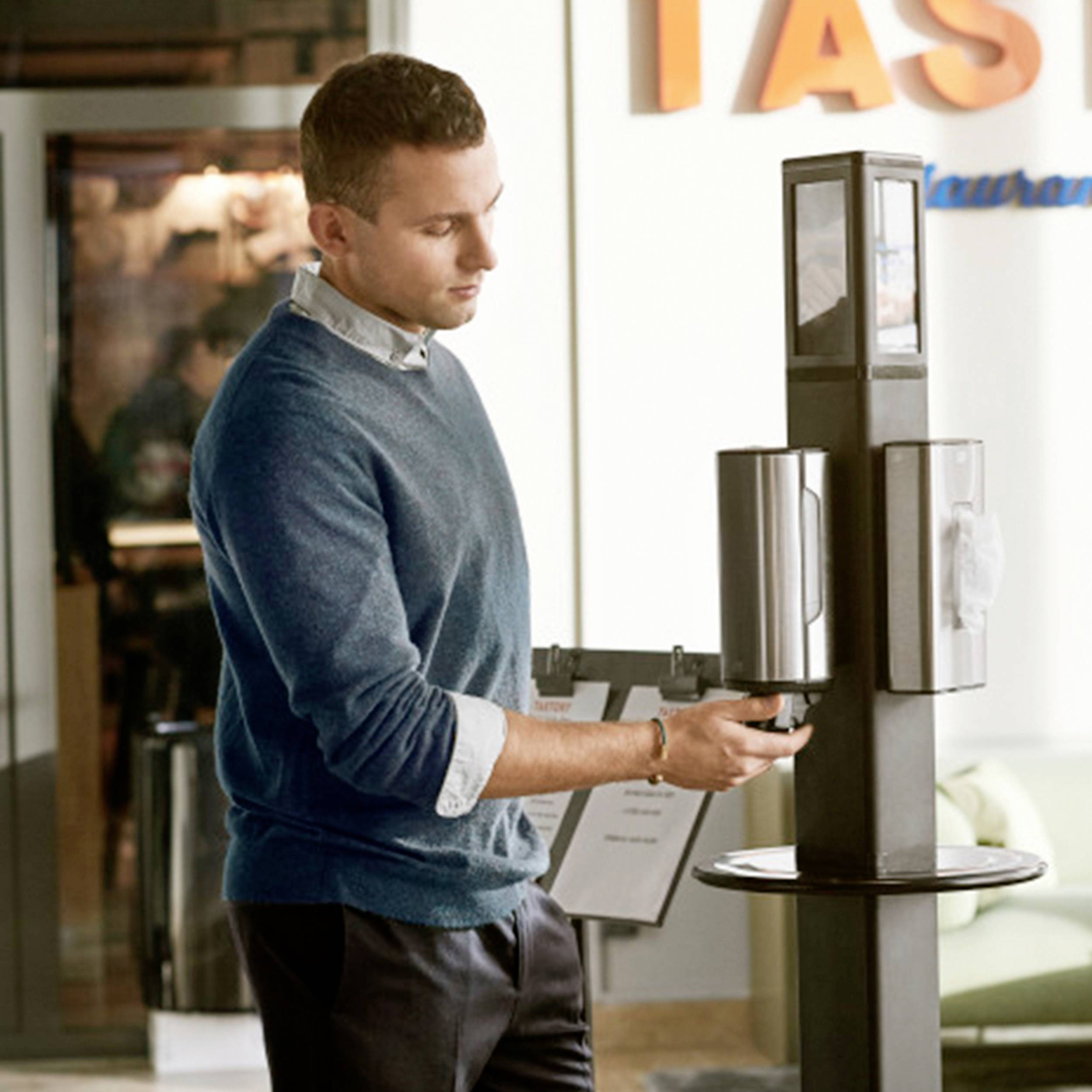 En person står i en modern restaurang och använder en beröringsfri handdesinfektionsdispenser.