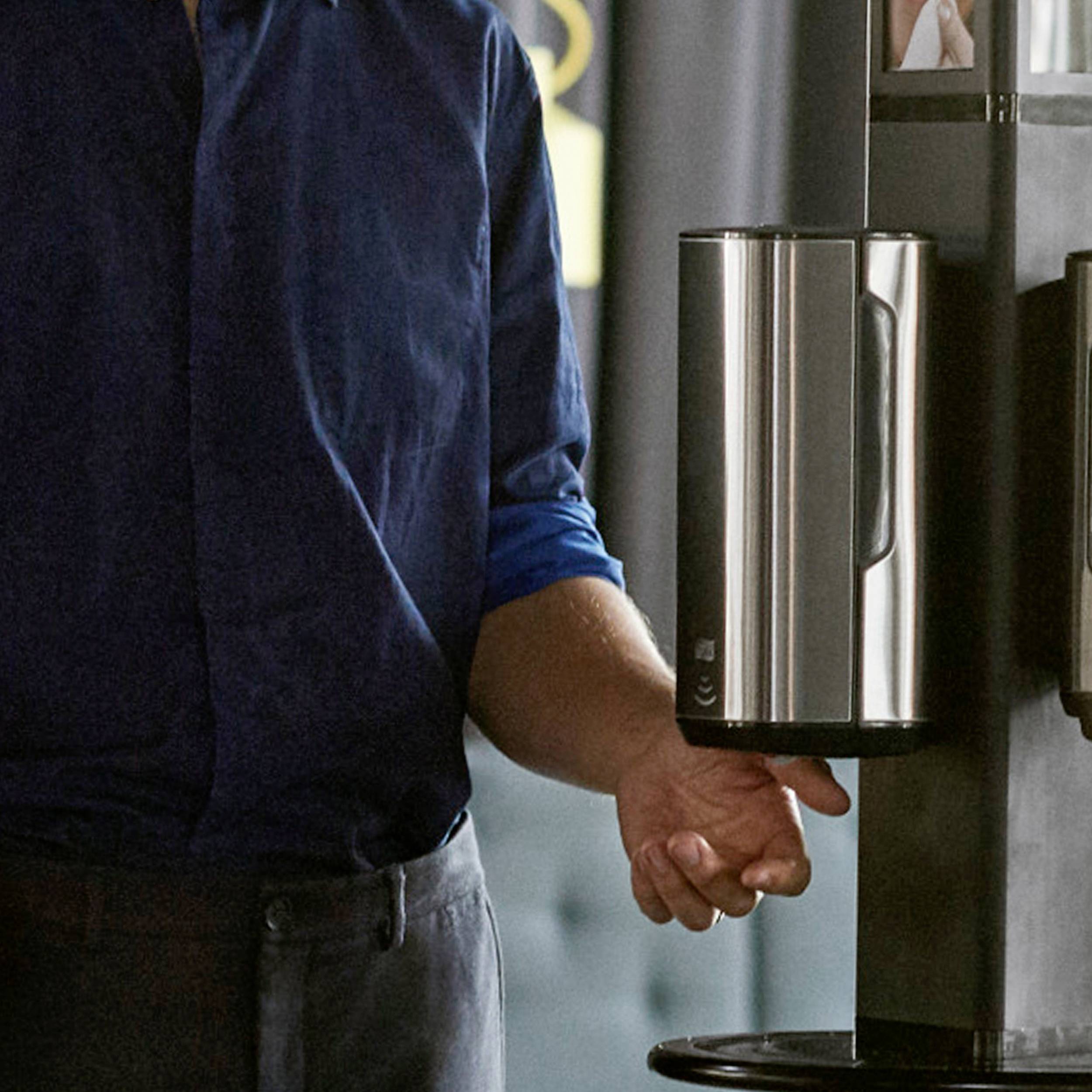 En person bär en blå skjorta och häller kaffe från en termos. I bakgrunden syns en hylla.