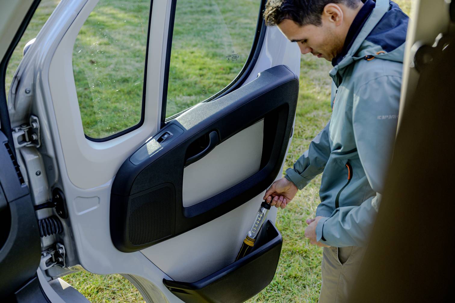 En man laddar en ficklampa i bildörrens ficka. I bakgrunden syns gräs, vilket tyder på en lantlig miljö.