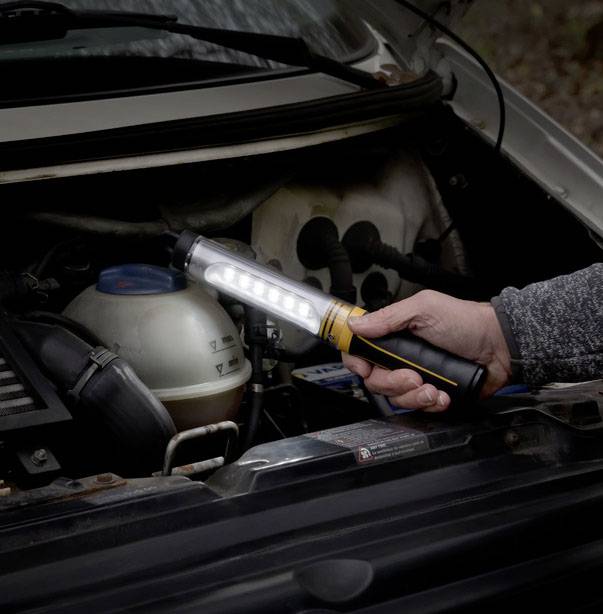 En person lyser med en bärbar lampa i ett bilserviceområde för att kunna se motorutrymmet bättre.