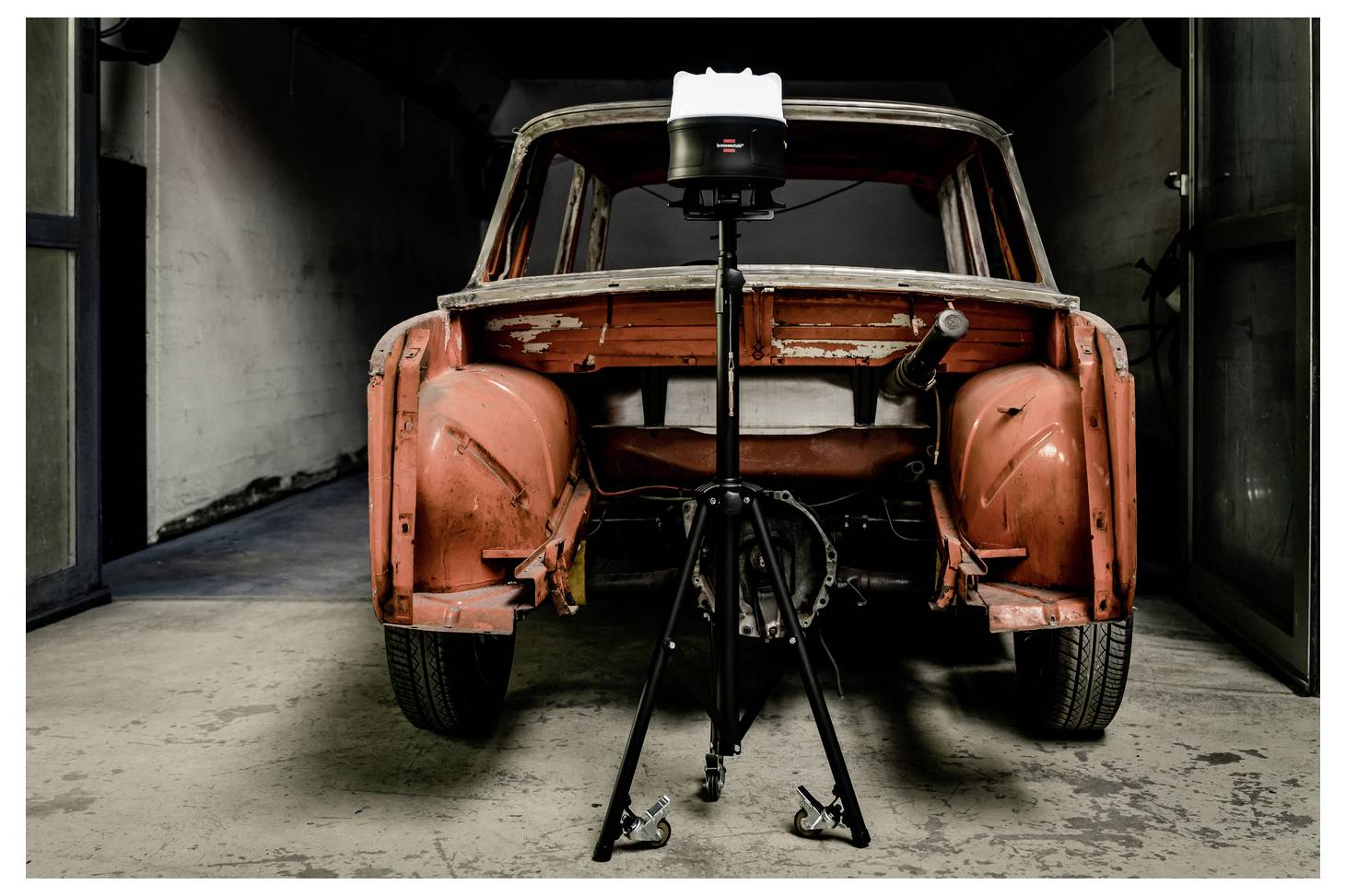 Frontvy av en avskuren orange vintage bilkaross på ett stativställ i ett garage, visar restaureringsarbete pågår.